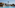 Resort swimming pool with water slides, palm tree, and thatched parasols.