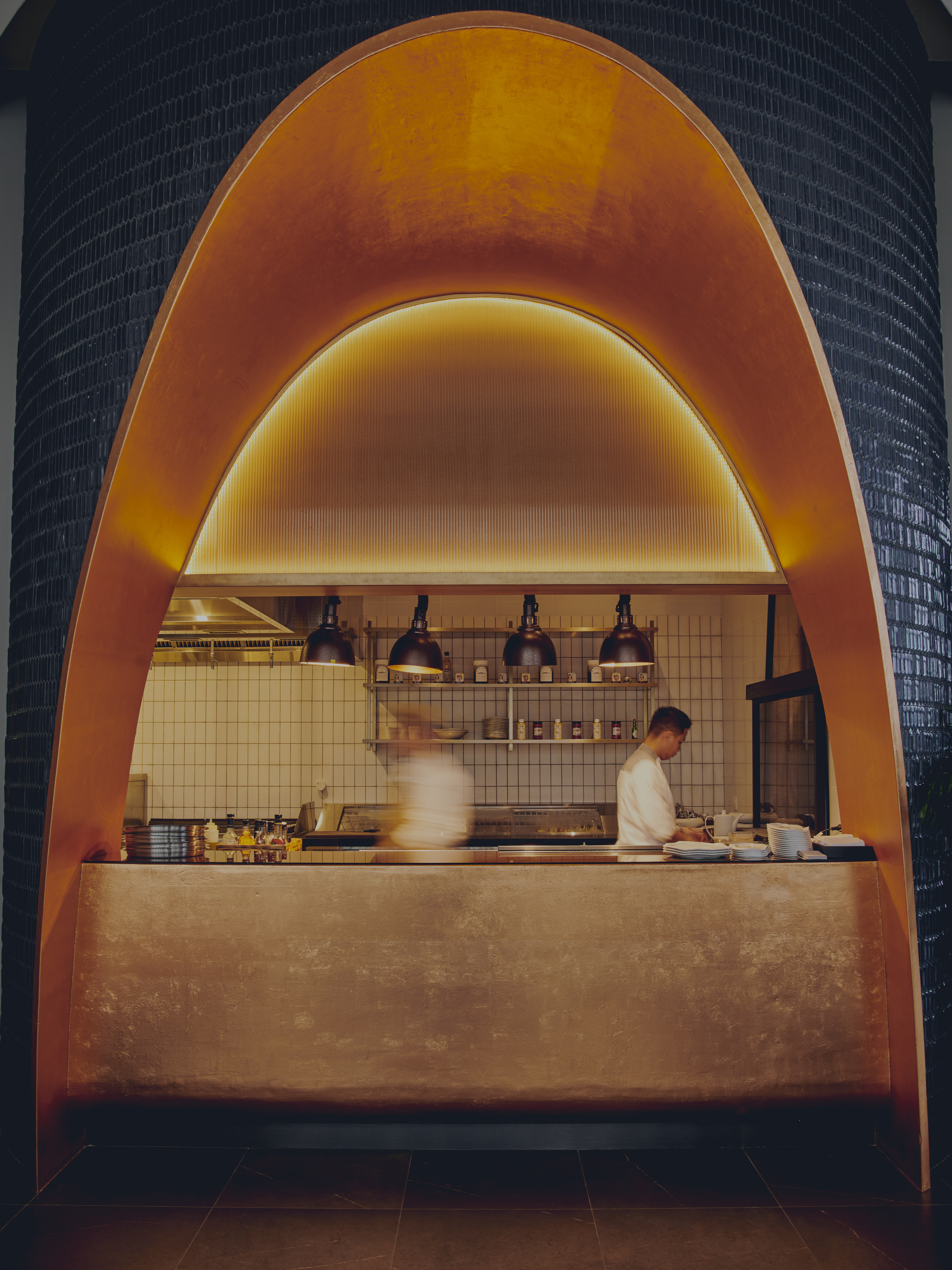 Chef in a modern open kitchen with glowing copper arch design.