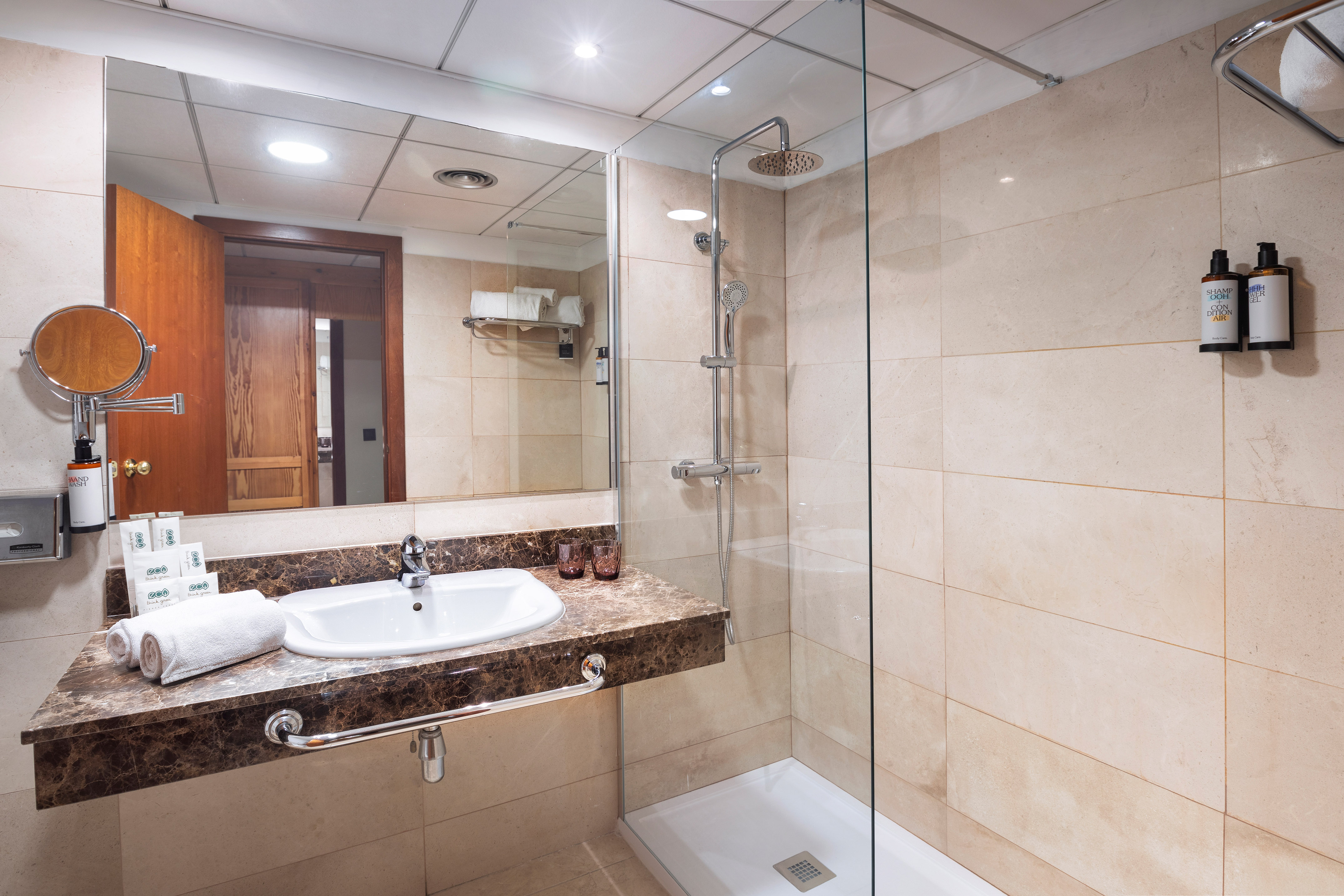 Modern hotel bathroom with walk-in shower, rain head, vanity sink, marble countertop.