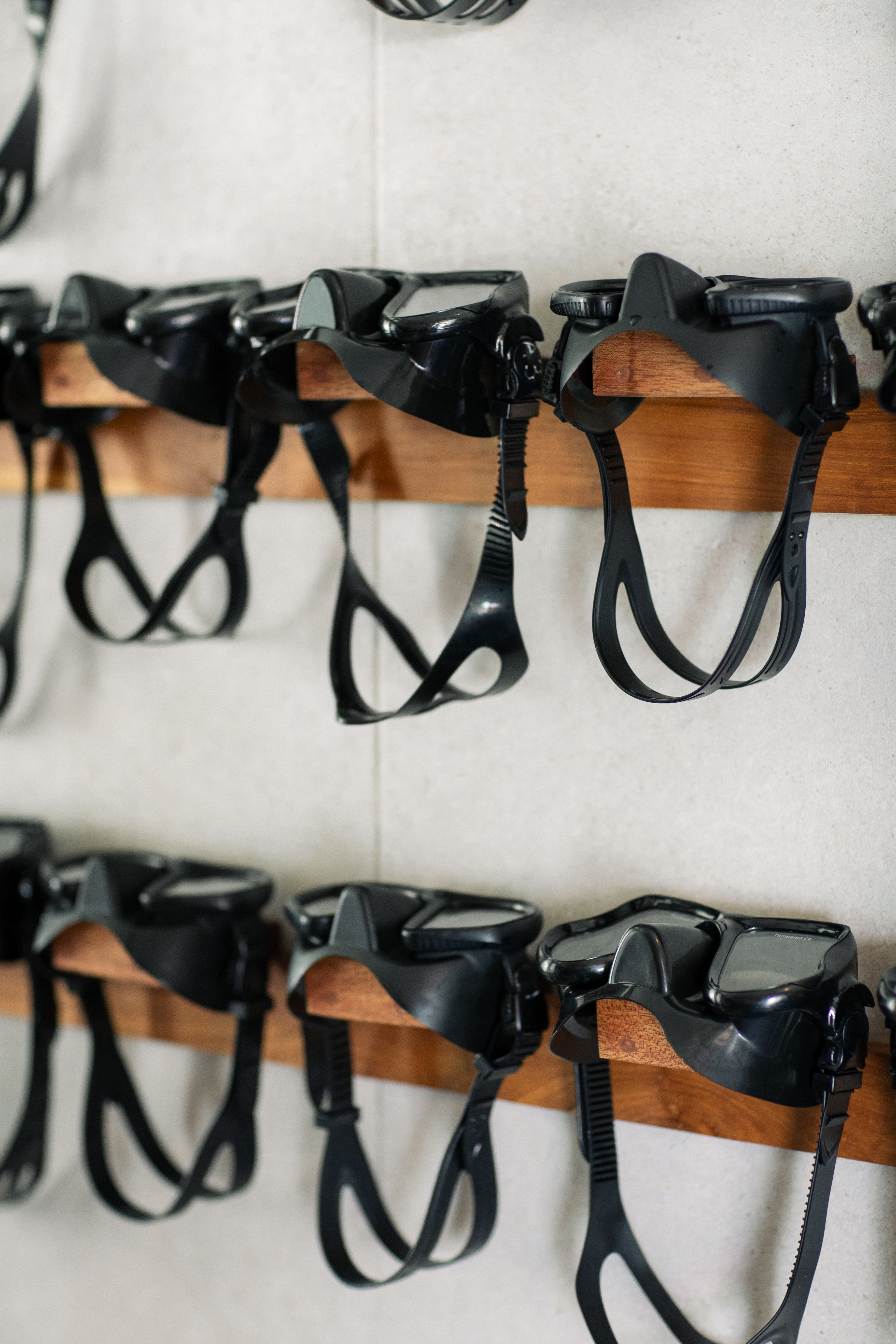 Black dive masks and snorkel gear with clear lenses hanging on wooden racks.