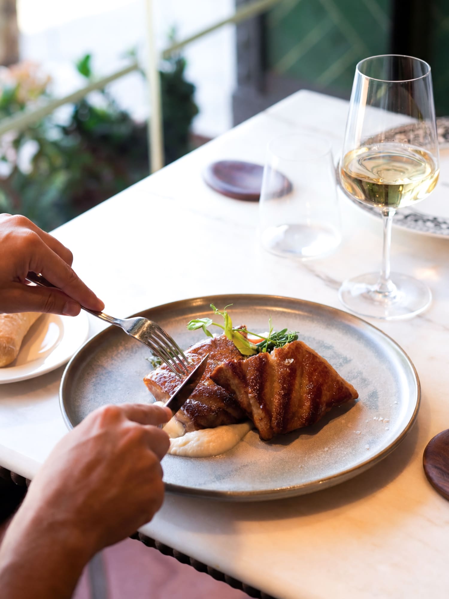 Person enjoying a gourmet meal with grilled meat and white wine.