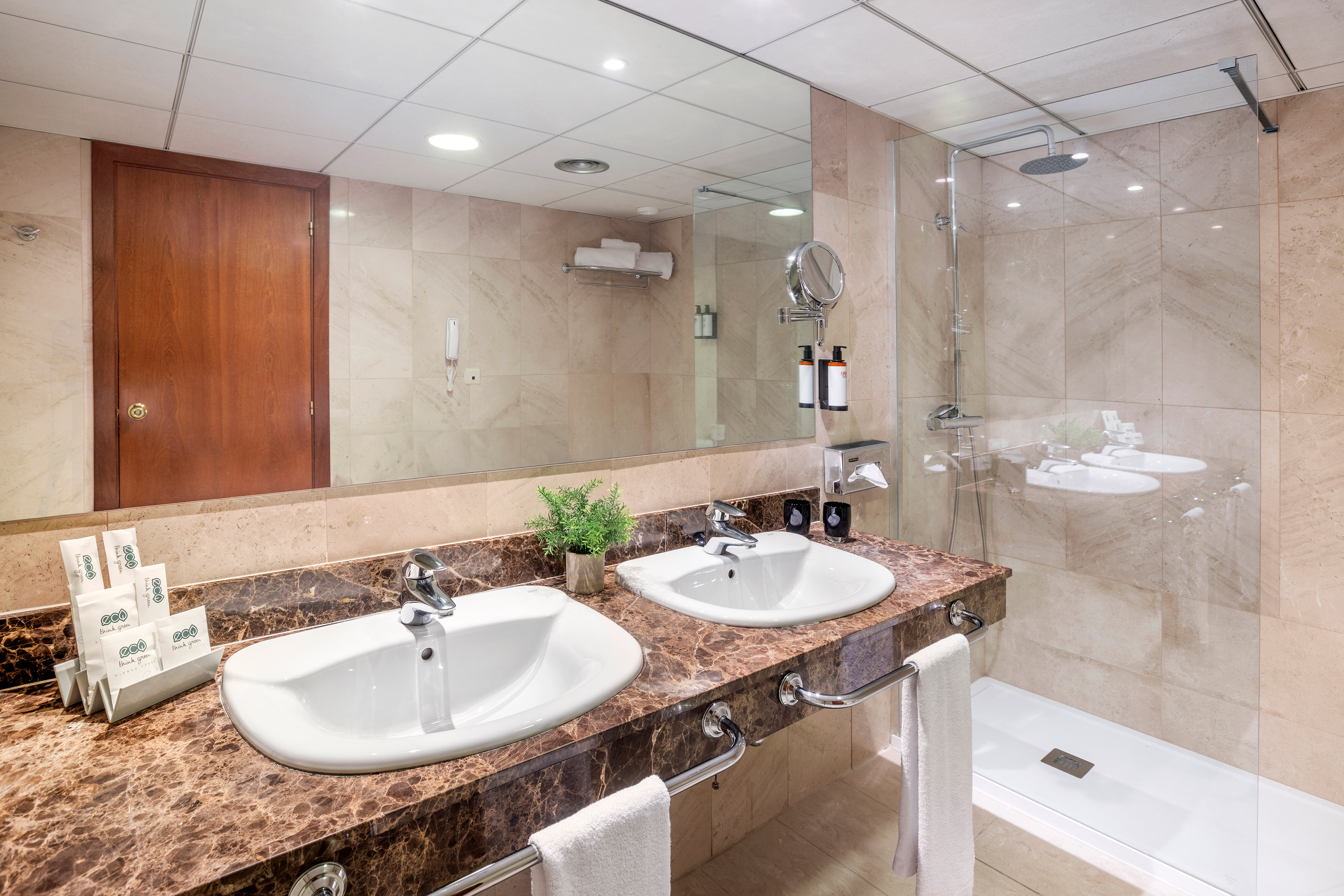 Modern hotel bathroom with dual sinks, brown marble vanity, mirror, and shower.