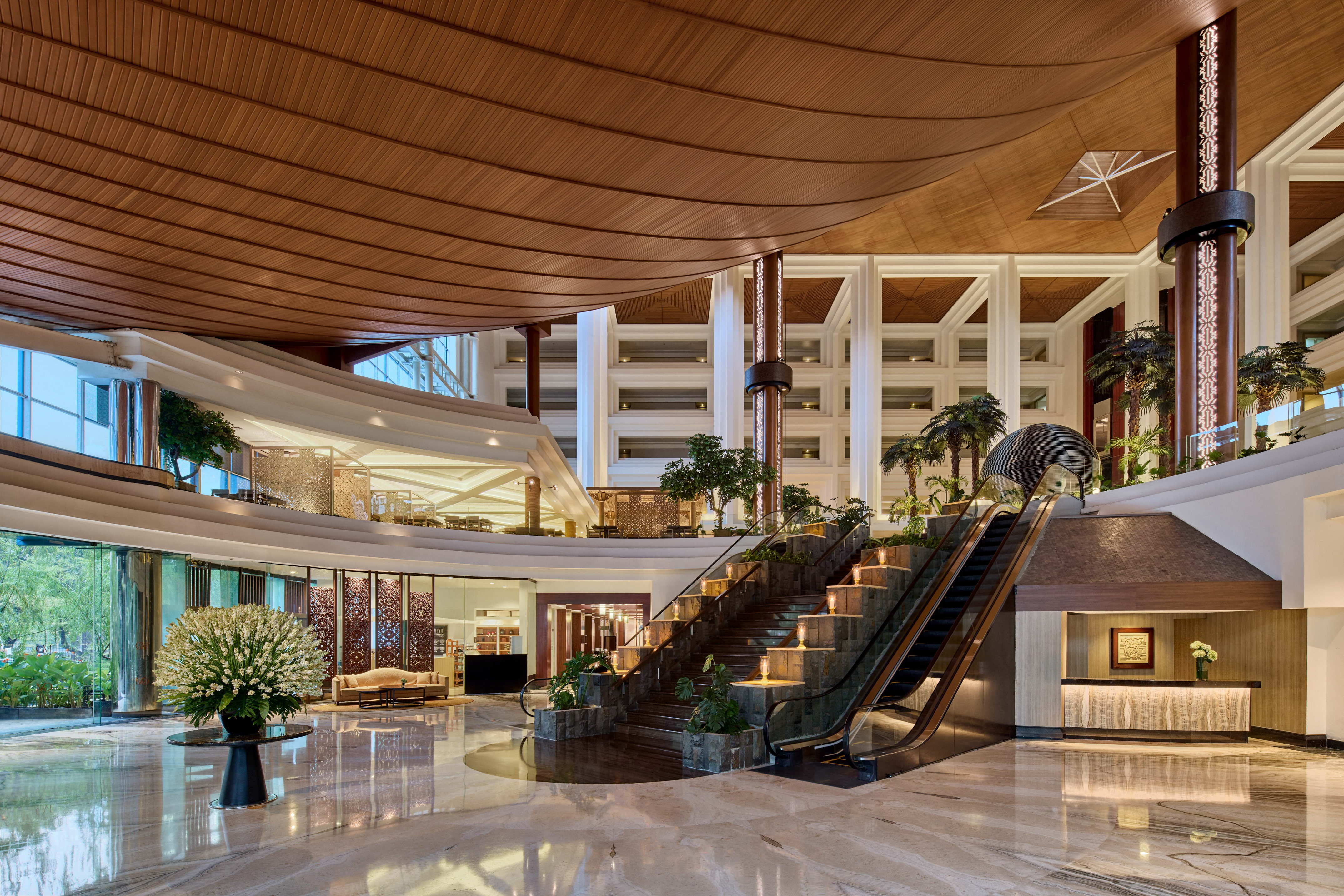 Luxury hotel lobby with grand staircase, escalator, and striking wooden ceiling.