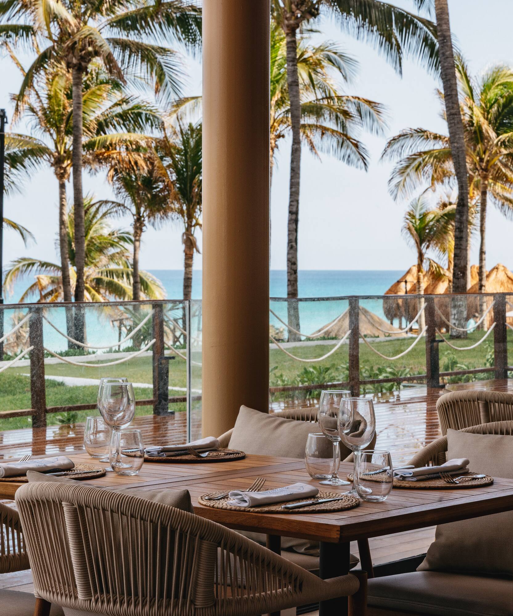 Beachfront dining area with set tables, palm trees, and ocean view.