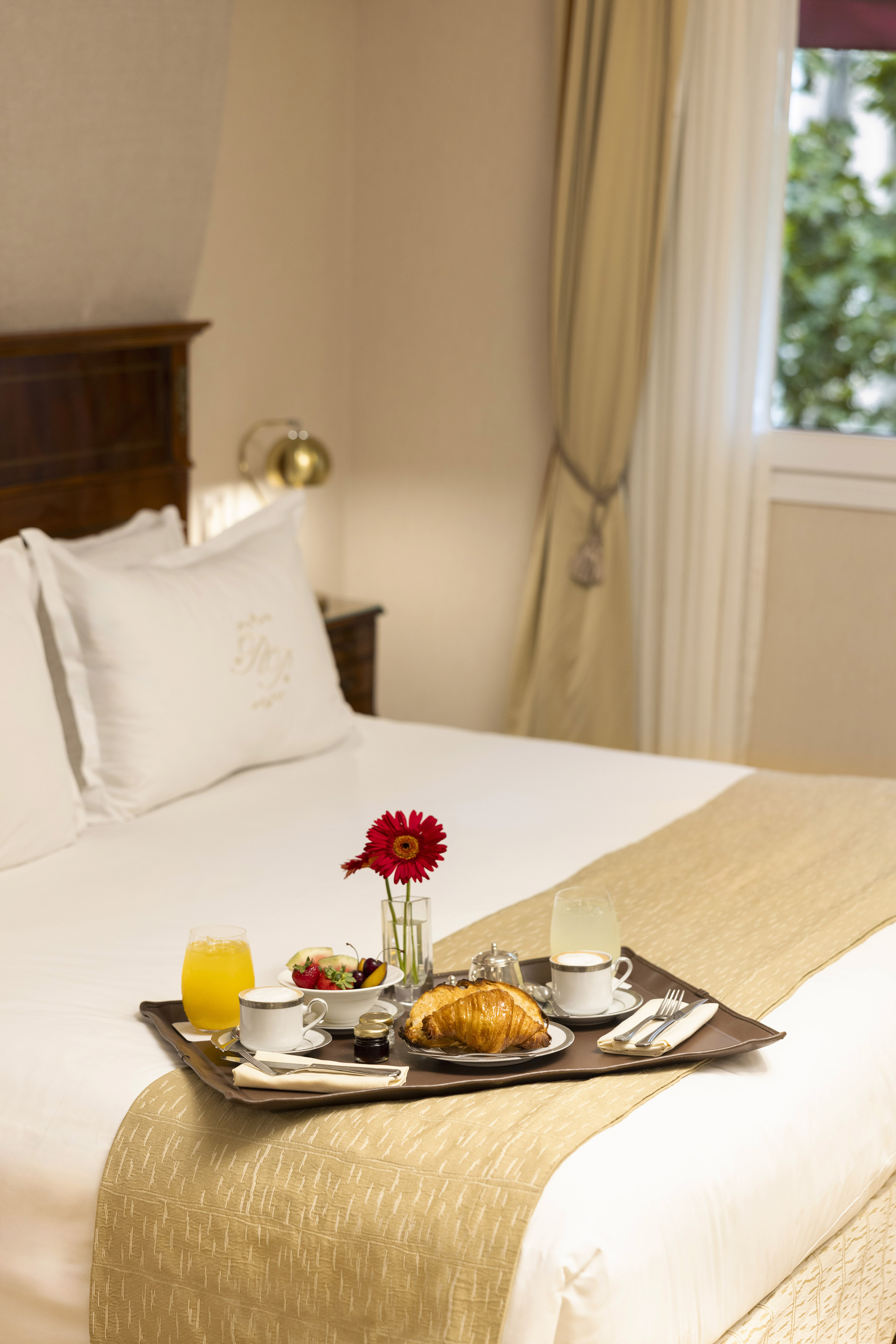 Breakfast in bed: croissants, coffee, juice, fruit, and flower on a hotel tray.