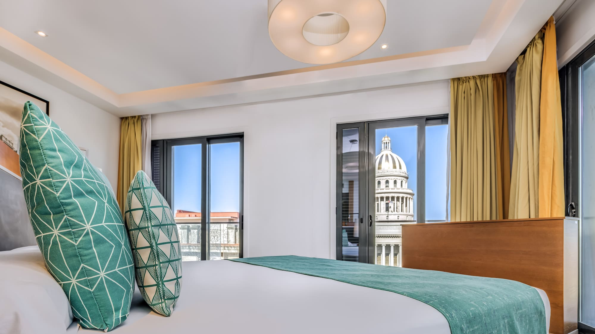 a bed with green pillows in a room with a large building in the background