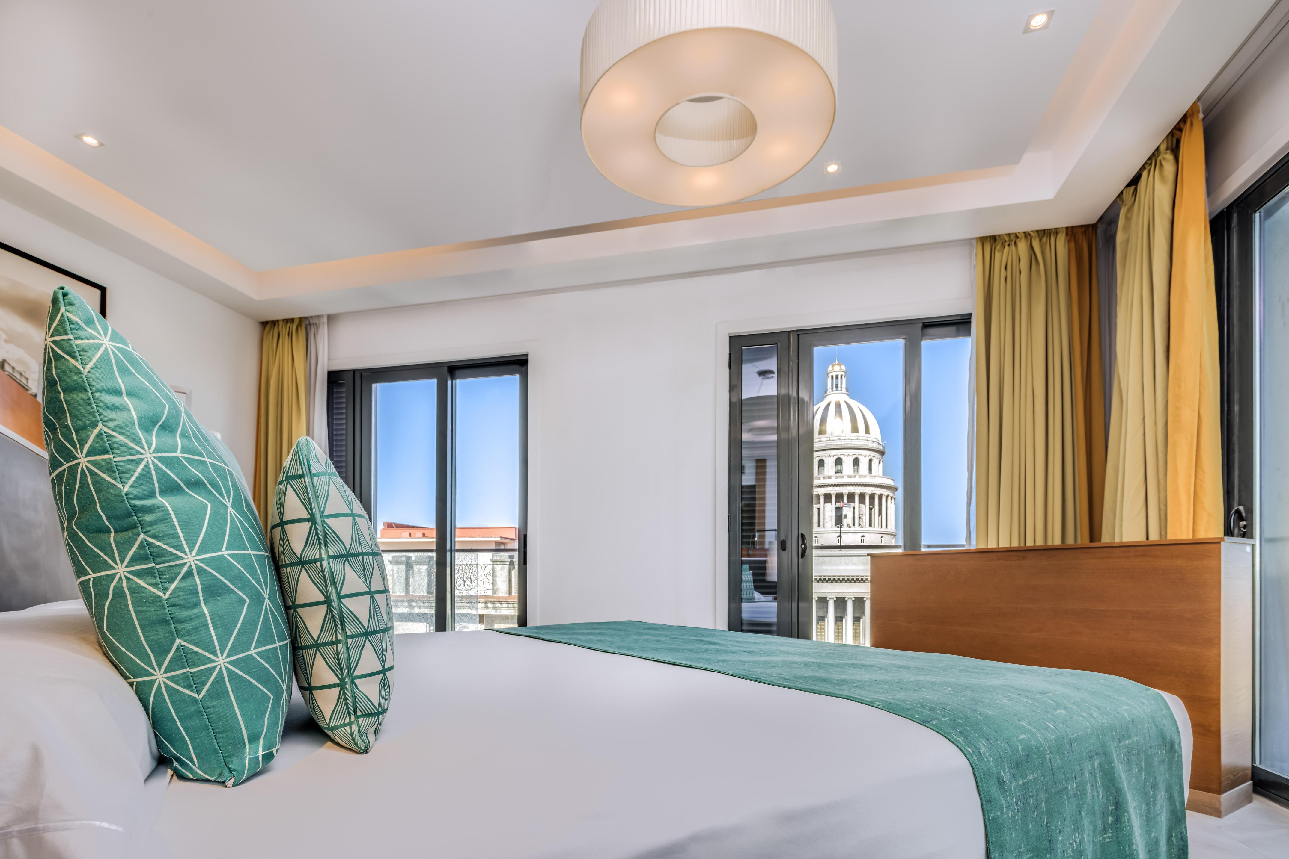 a bed with green pillows in a room with a large building in the background