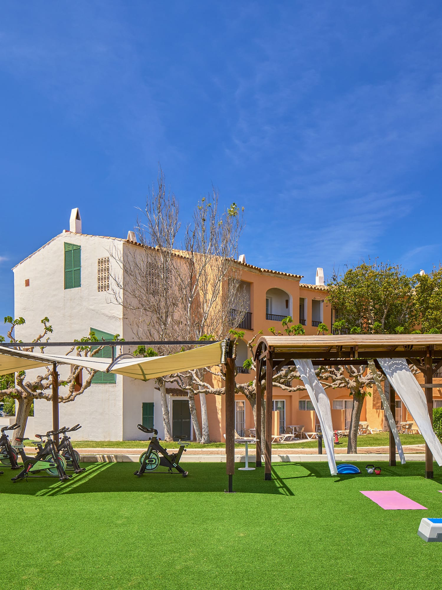 Outdoor resort gym: spinning bikes, yoga mats, and fitness equipment on turf.