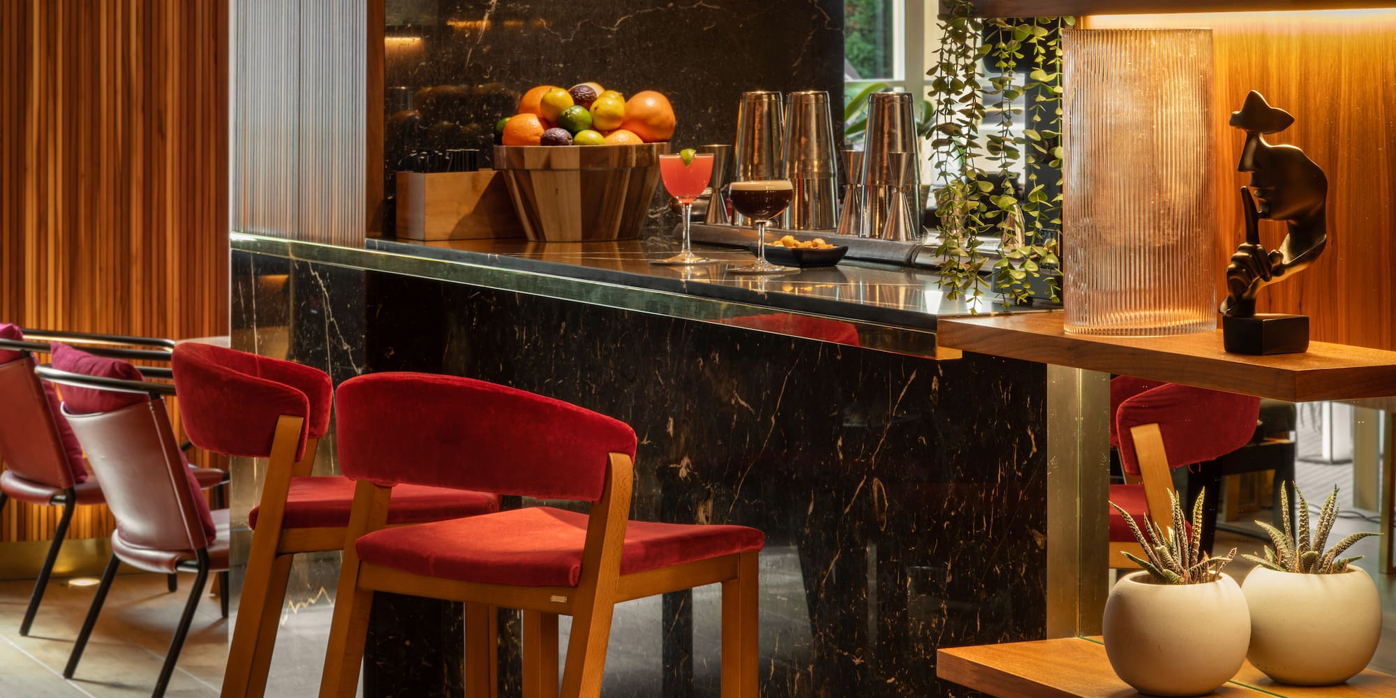 Modern luxury hotel bar with black marble counter, red velvet stools, and cocktails.