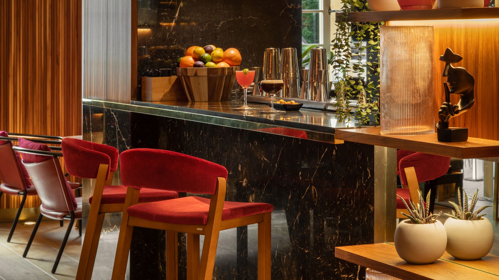 Modern luxury hotel bar with black marble counter, red velvet stools, and cocktails.
