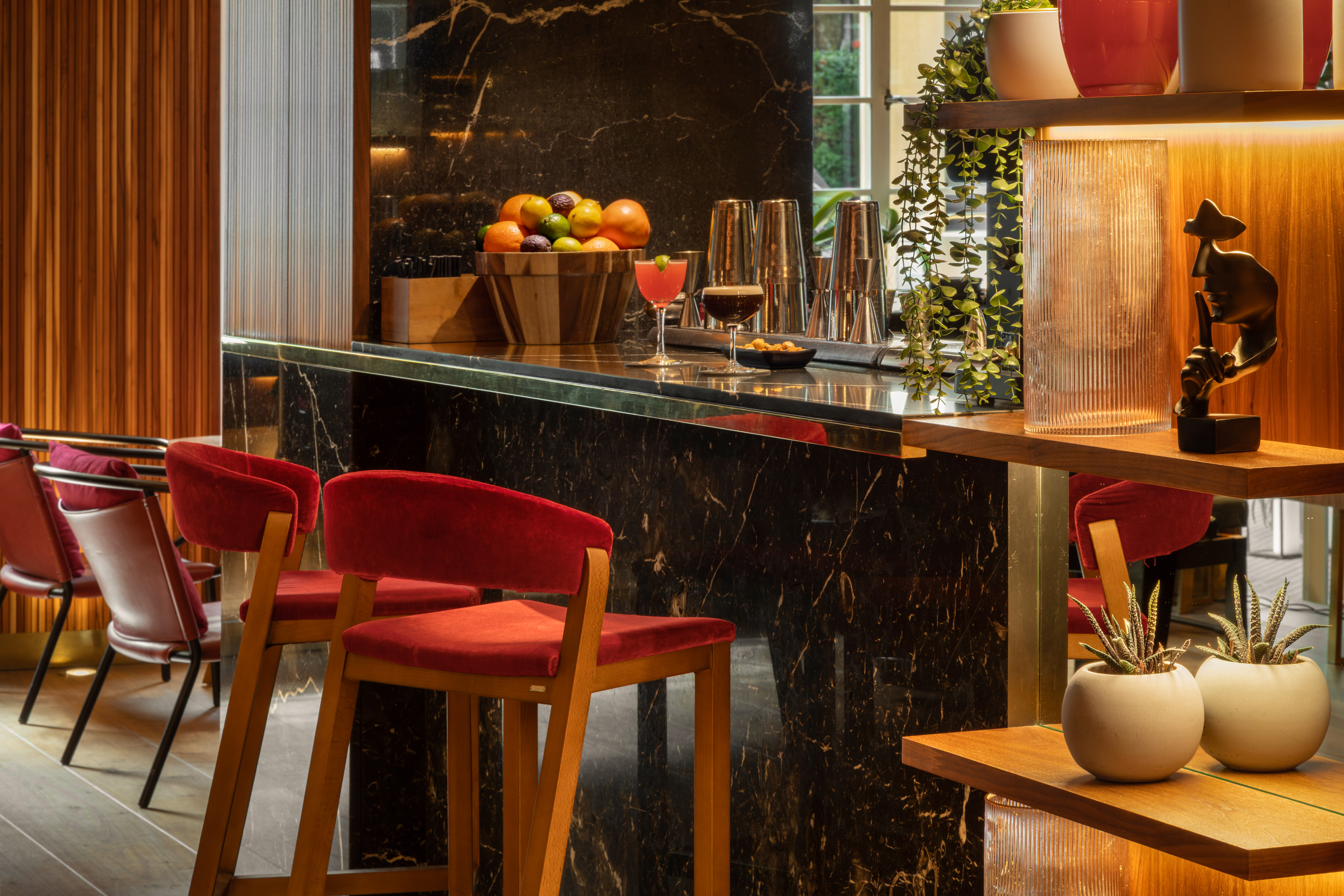 Modern luxury hotel bar with black marble counter, red velvet stools, and cocktails.