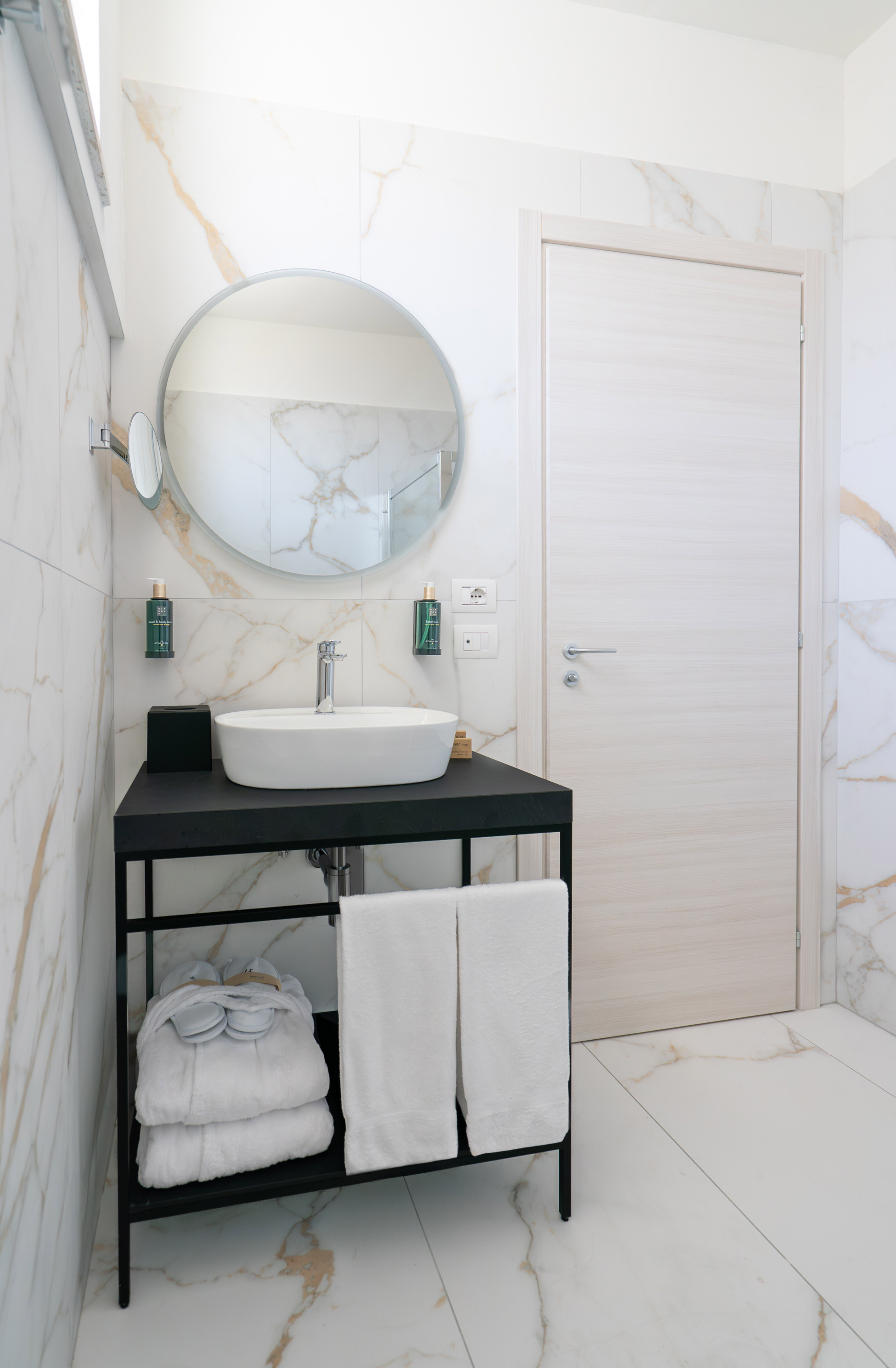 Modern white marble bathroom with black vanity, vessel sink, and round mirror.