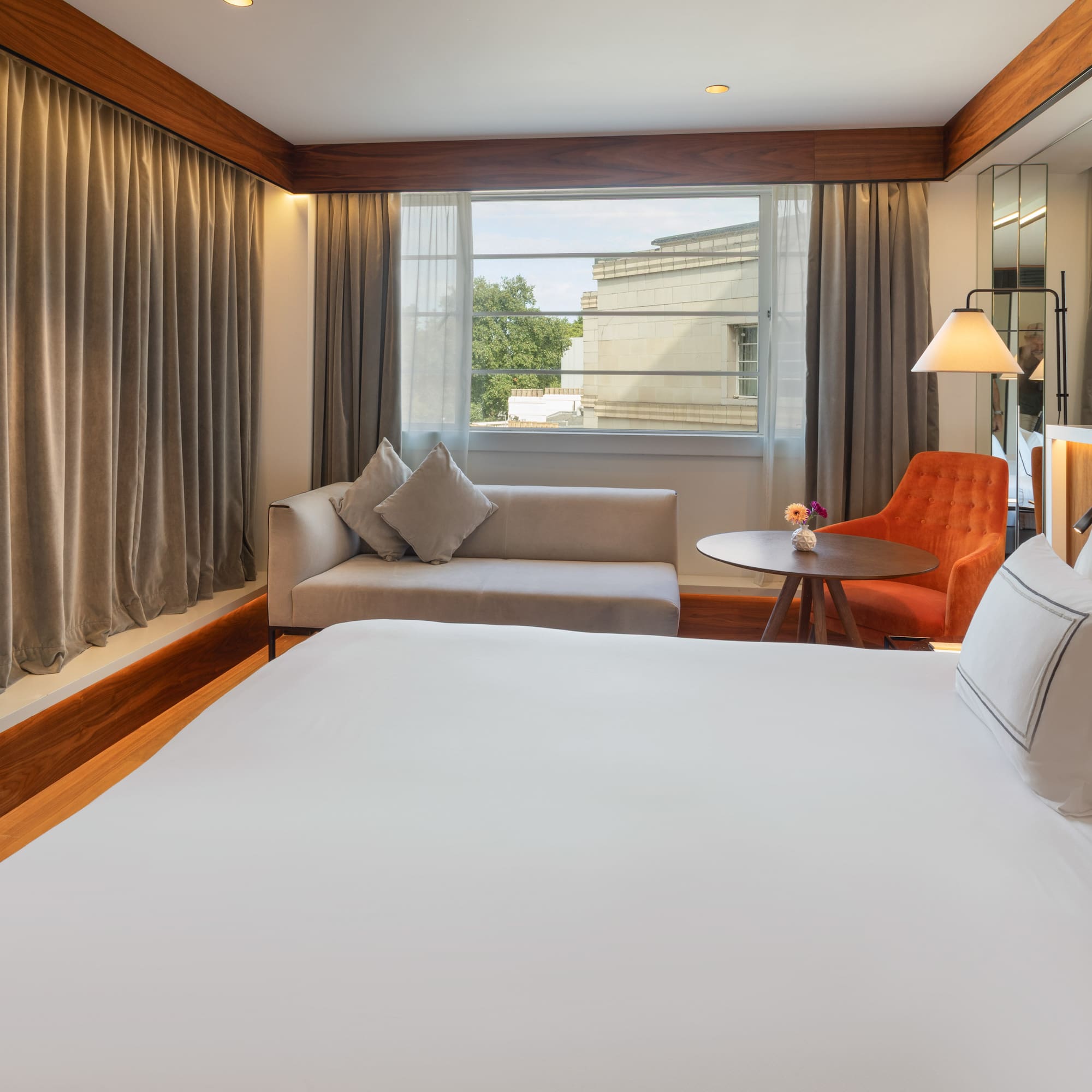 Modern hotel room with king bed, sofa, orange armchair, and giraffe art.