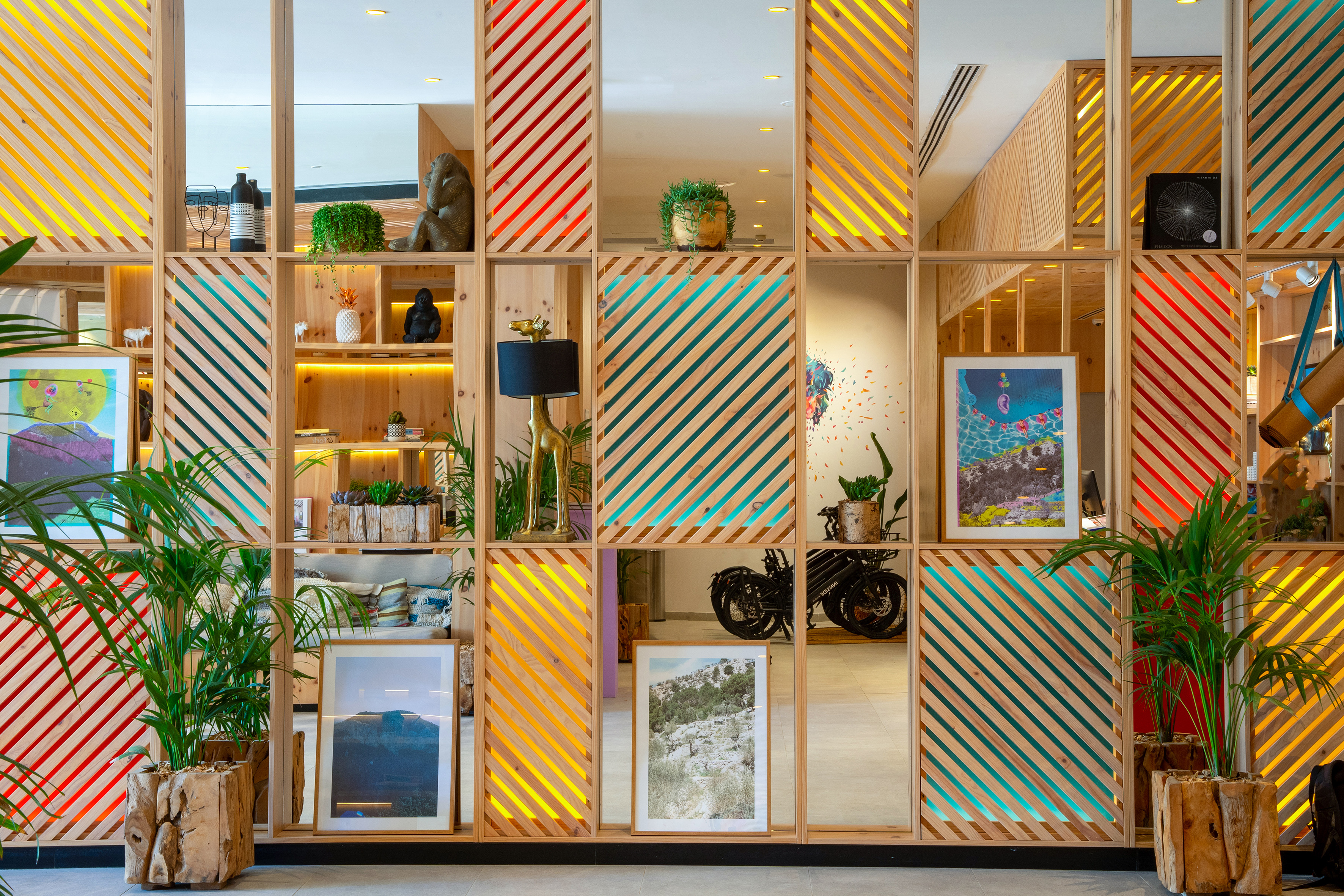 Colorful wooden room divider with diagonal slats, mirrors, plants, and decor.