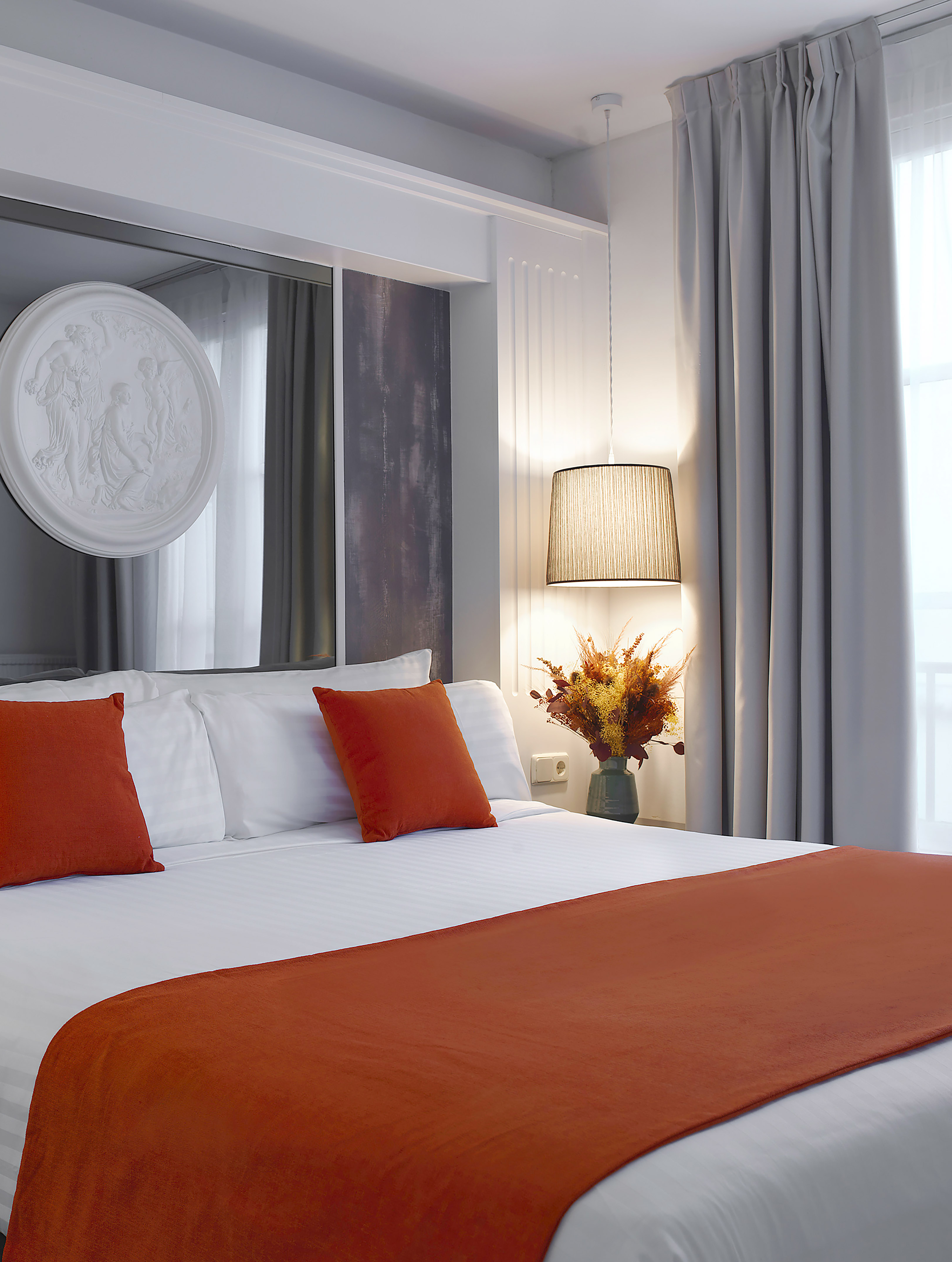 Modern bedroom with white bed, orange throw and pillows, classic relief art.