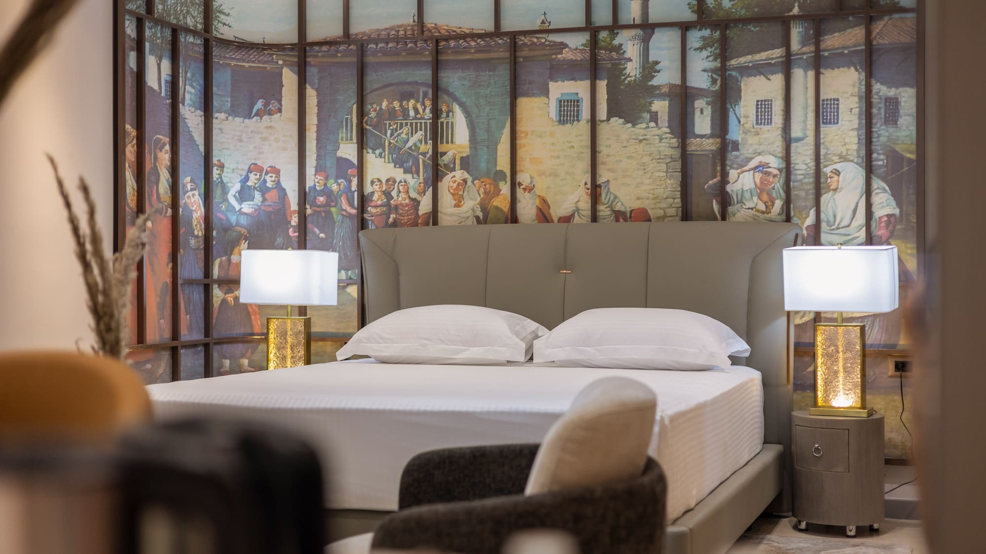 Bedroom with grey bed, white linens, and traditional village mural.