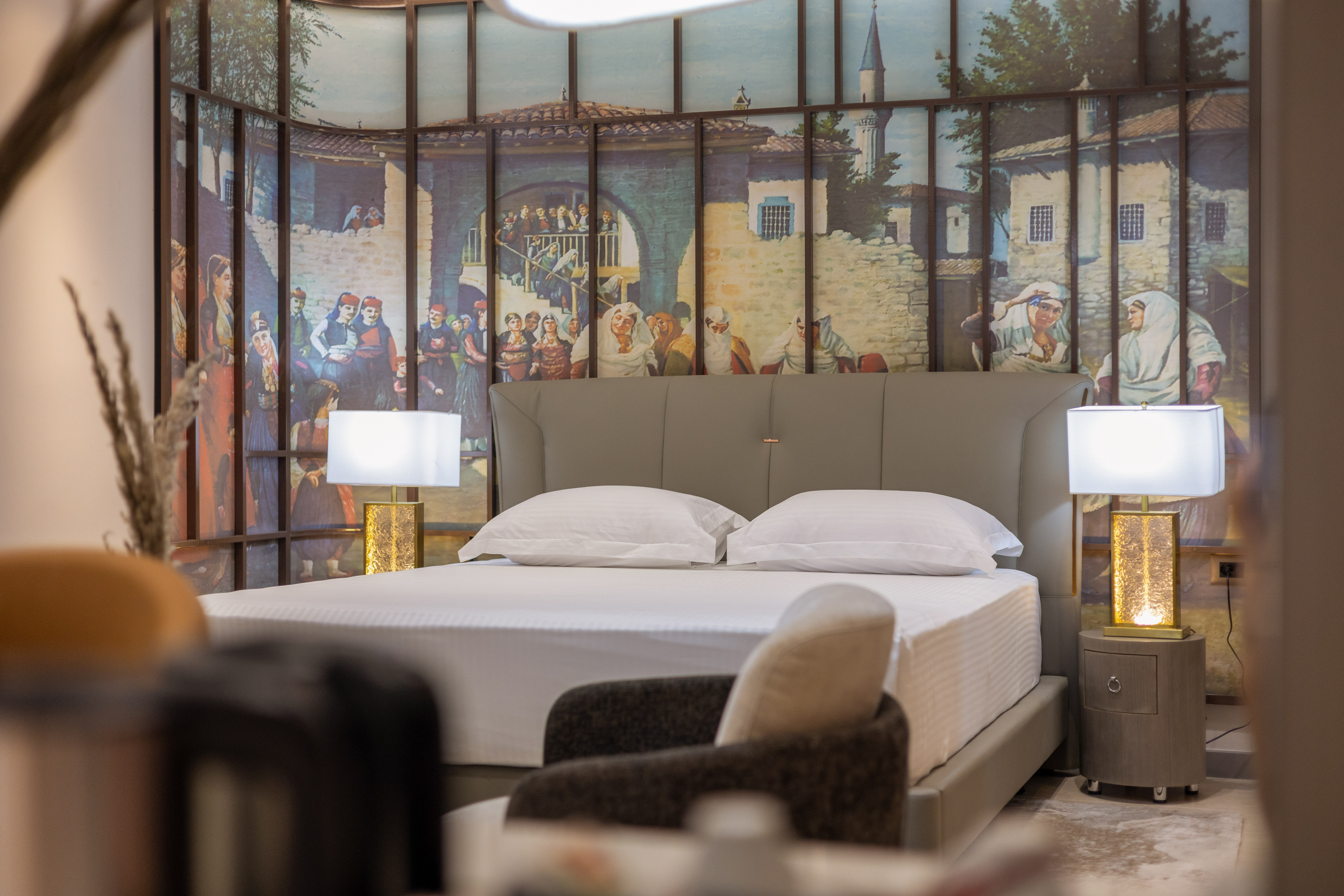 Bedroom with grey bed, white linens, and traditional village mural.