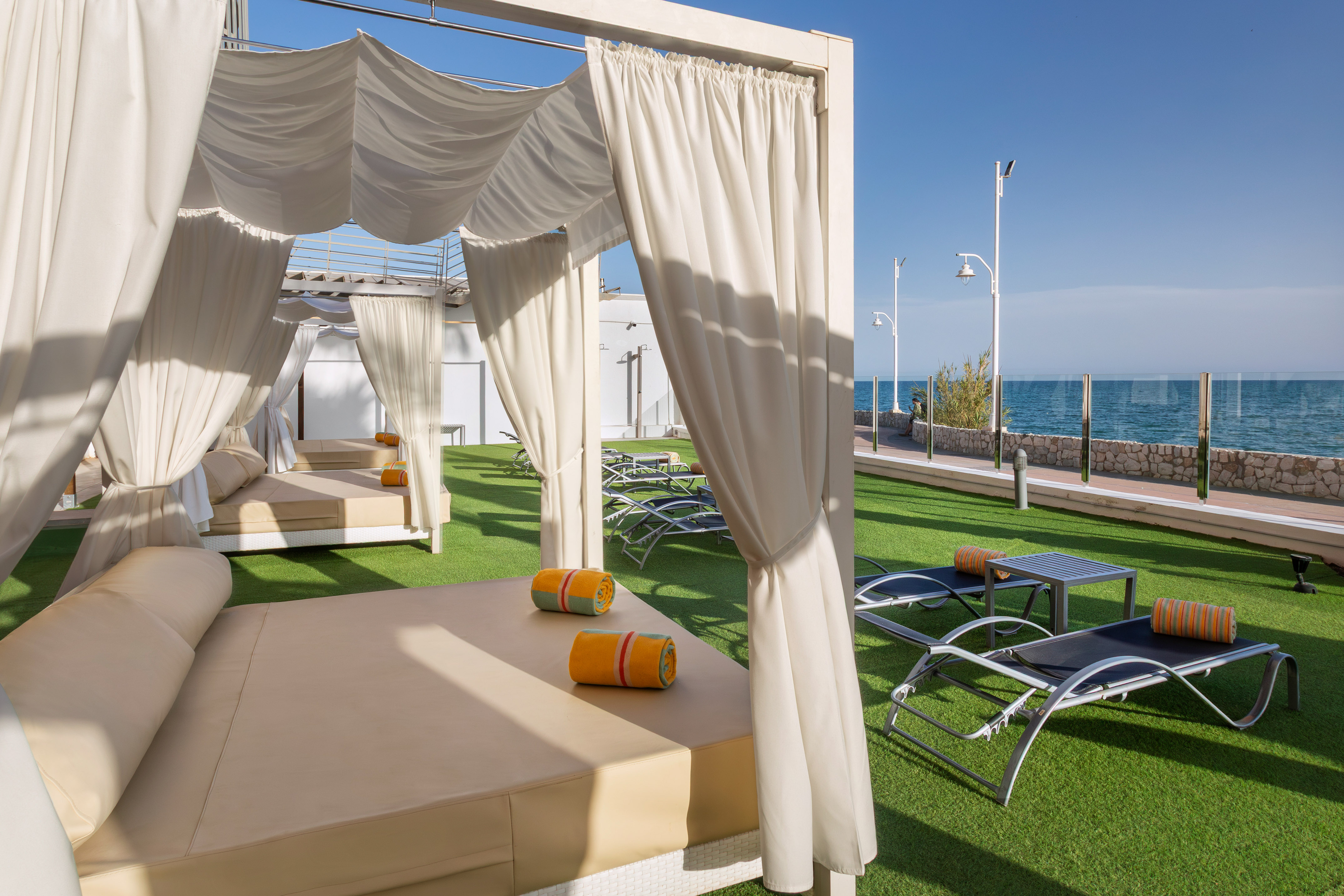 White cabanas and lounge beds on artificial grass with ocean view.