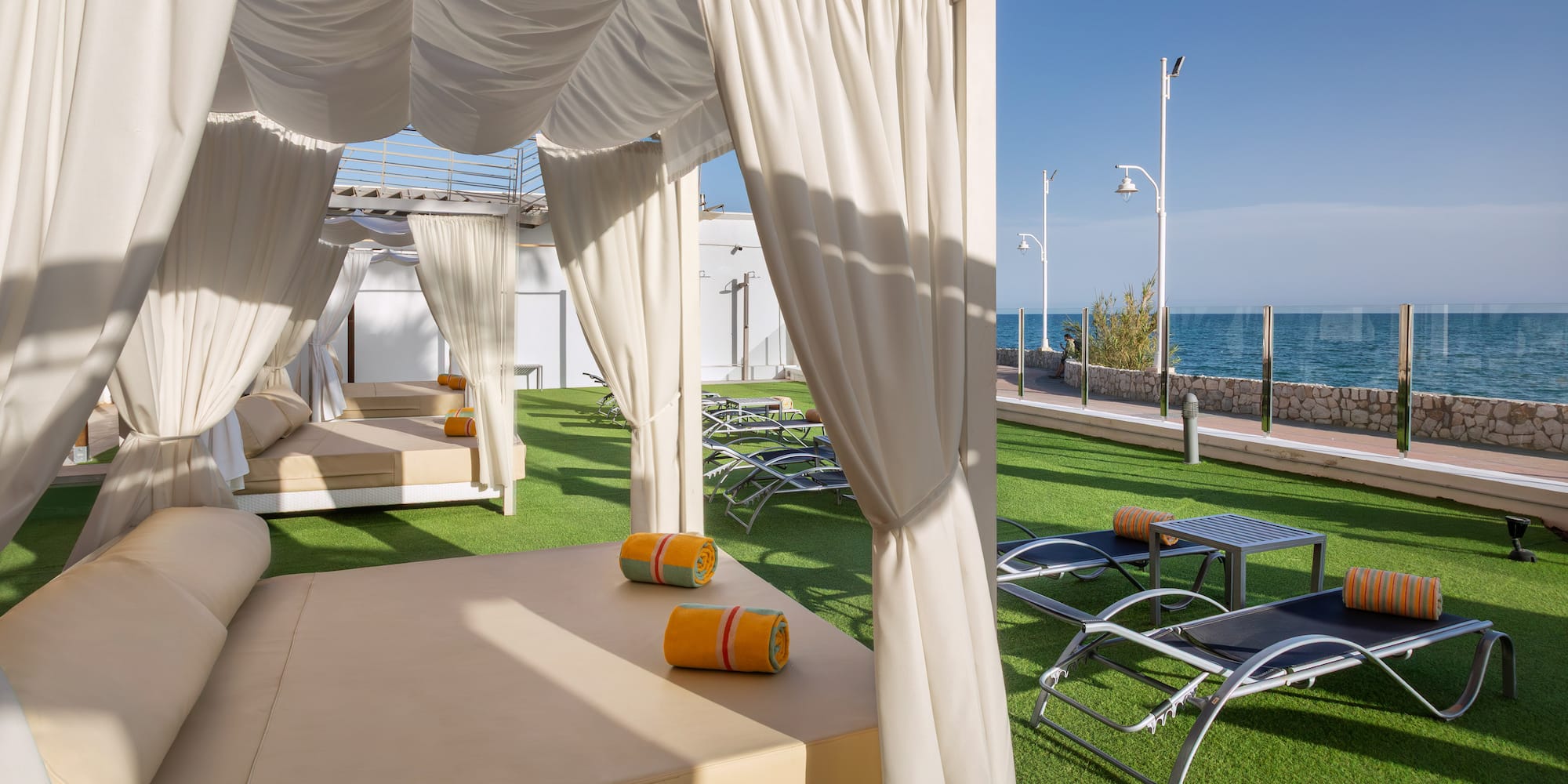 White cabanas and lounge beds on artificial grass with ocean view.