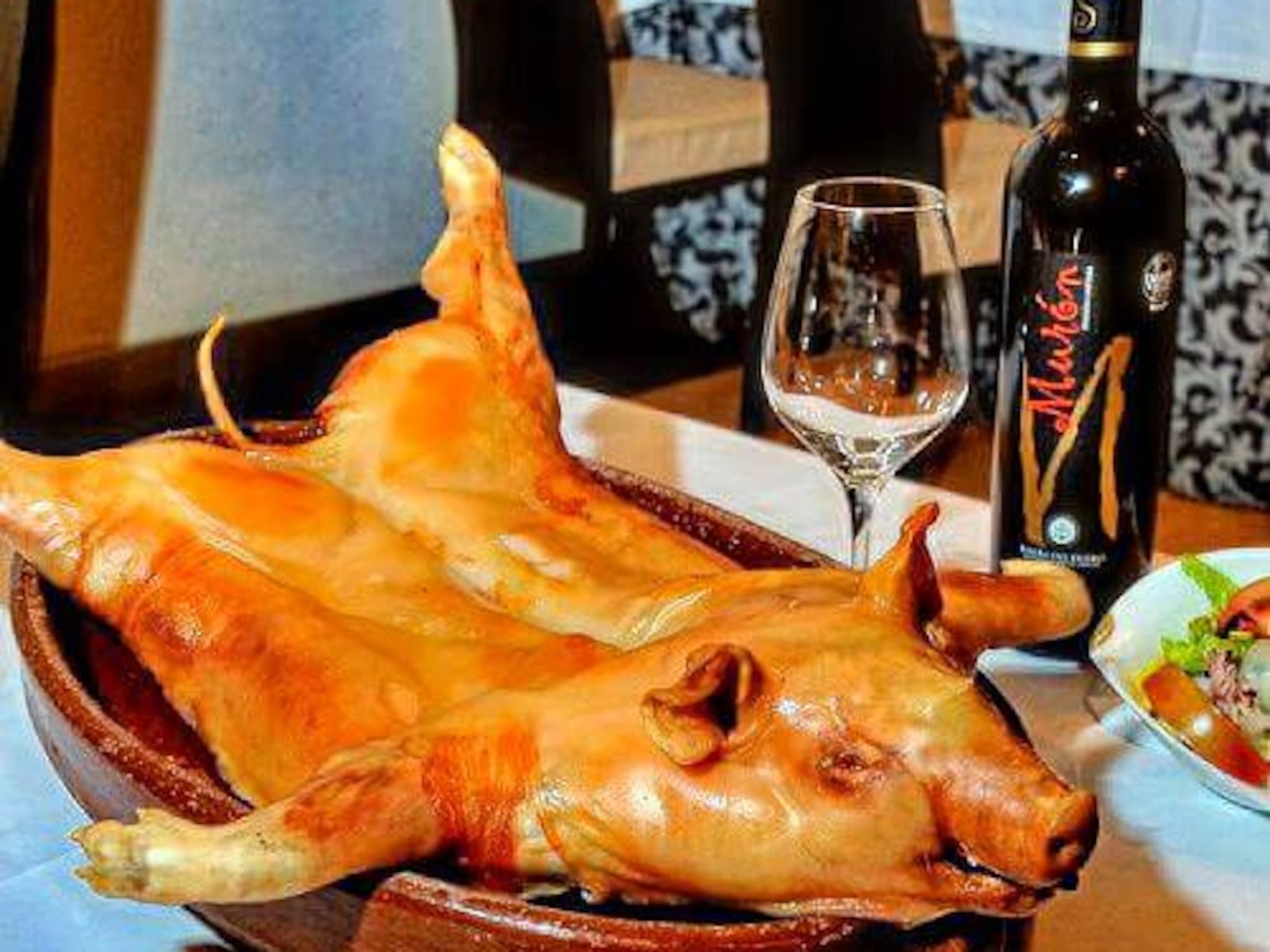 A pig's head sits on a plate beside a bottle of wine.