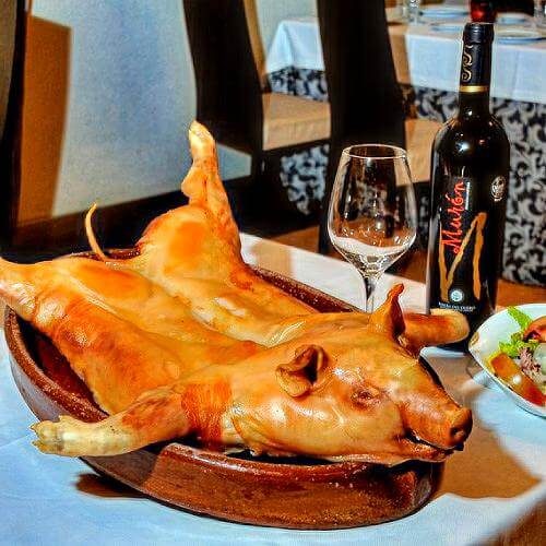 A pig's head sits on a plate beside a bottle of wine.