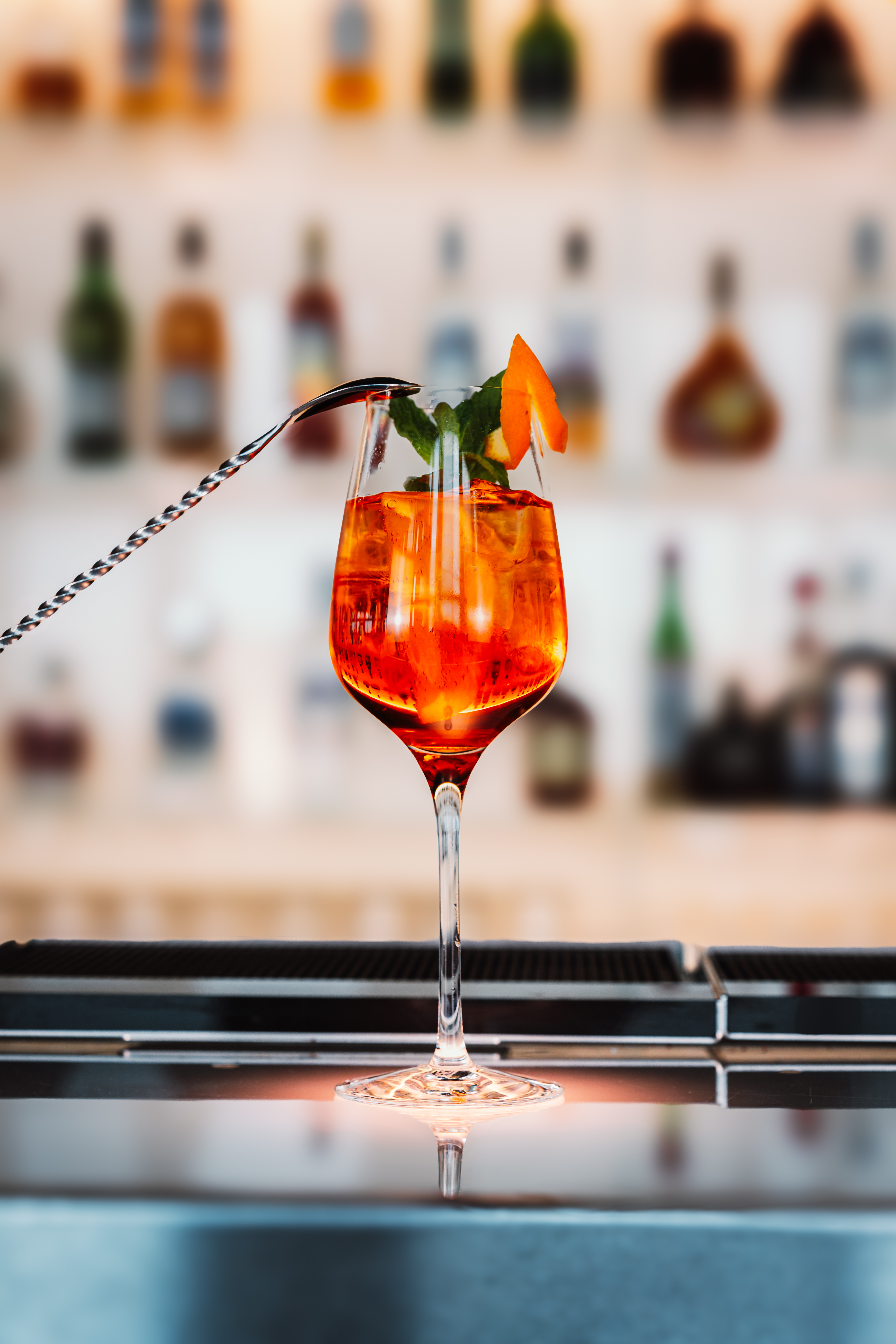 Orange cocktail with mint, orange peel, and stirring spoon at a bar.