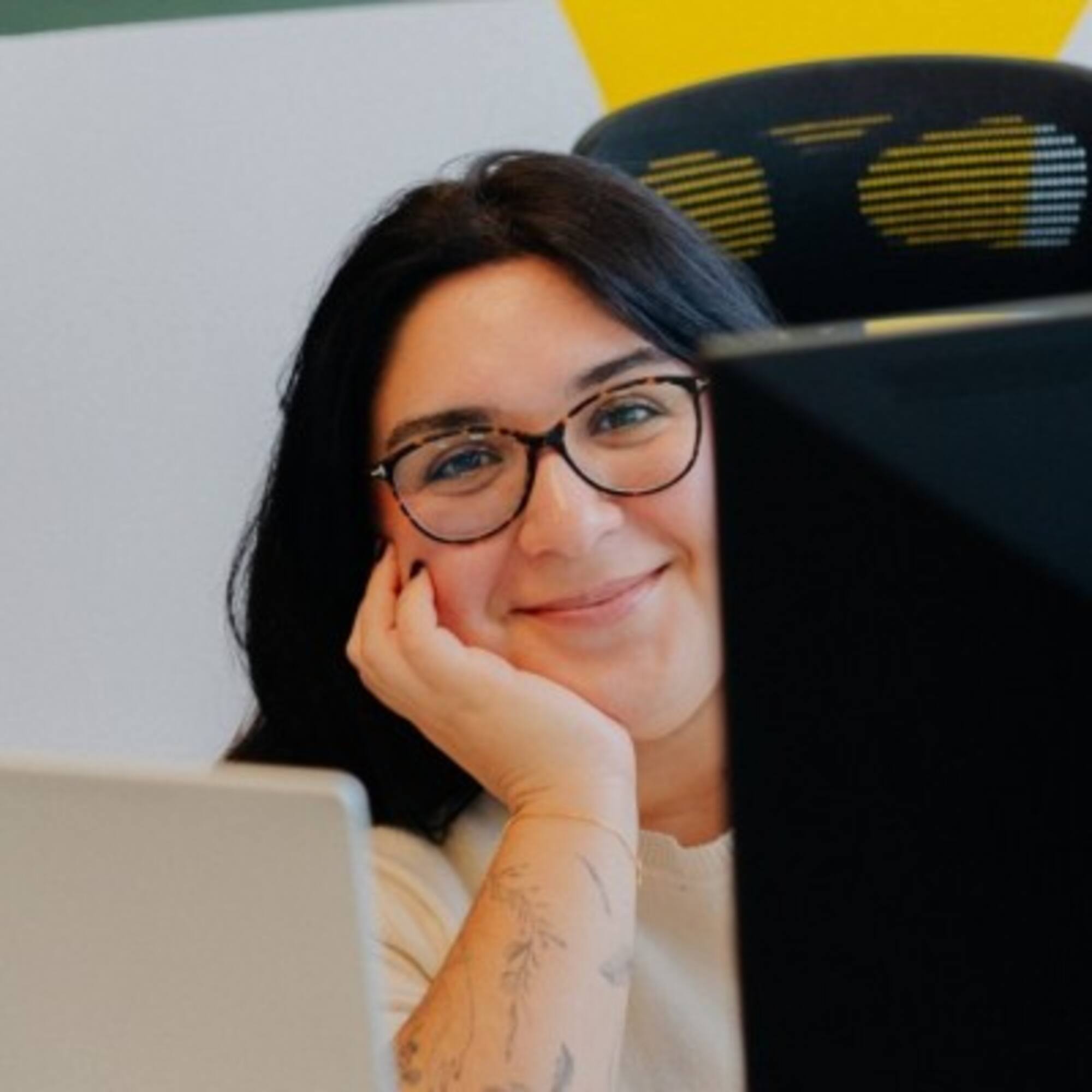 Professional woman with glasses smiling, working at office computer.