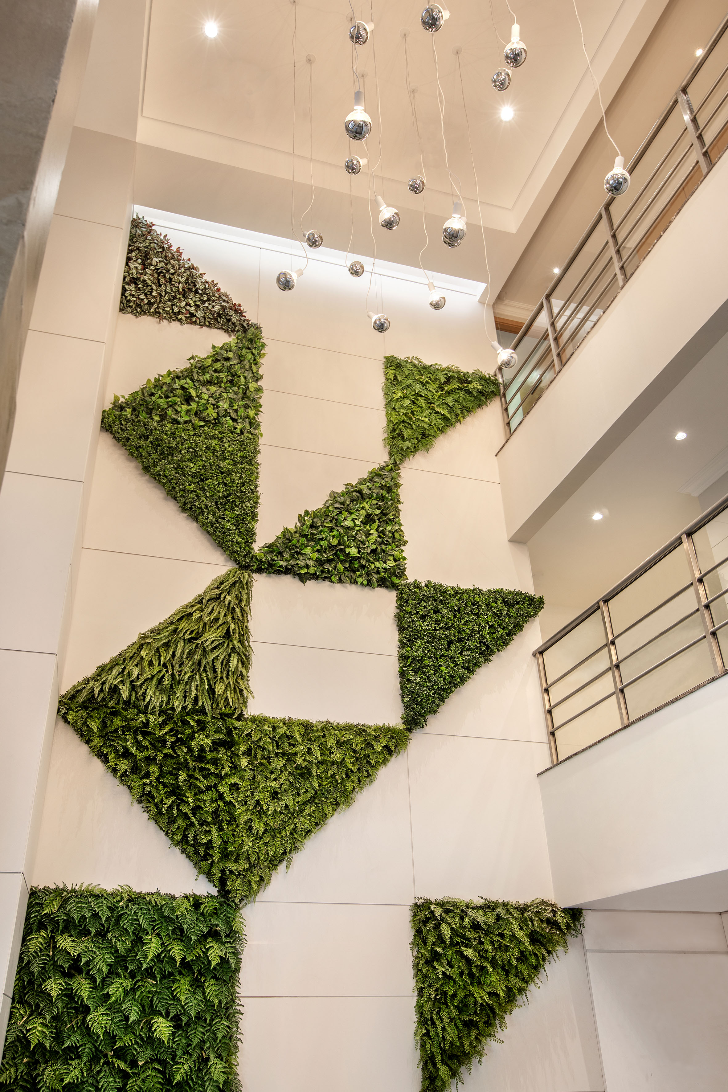 Modern geometric living wall on white interior, lit by pendant lights.