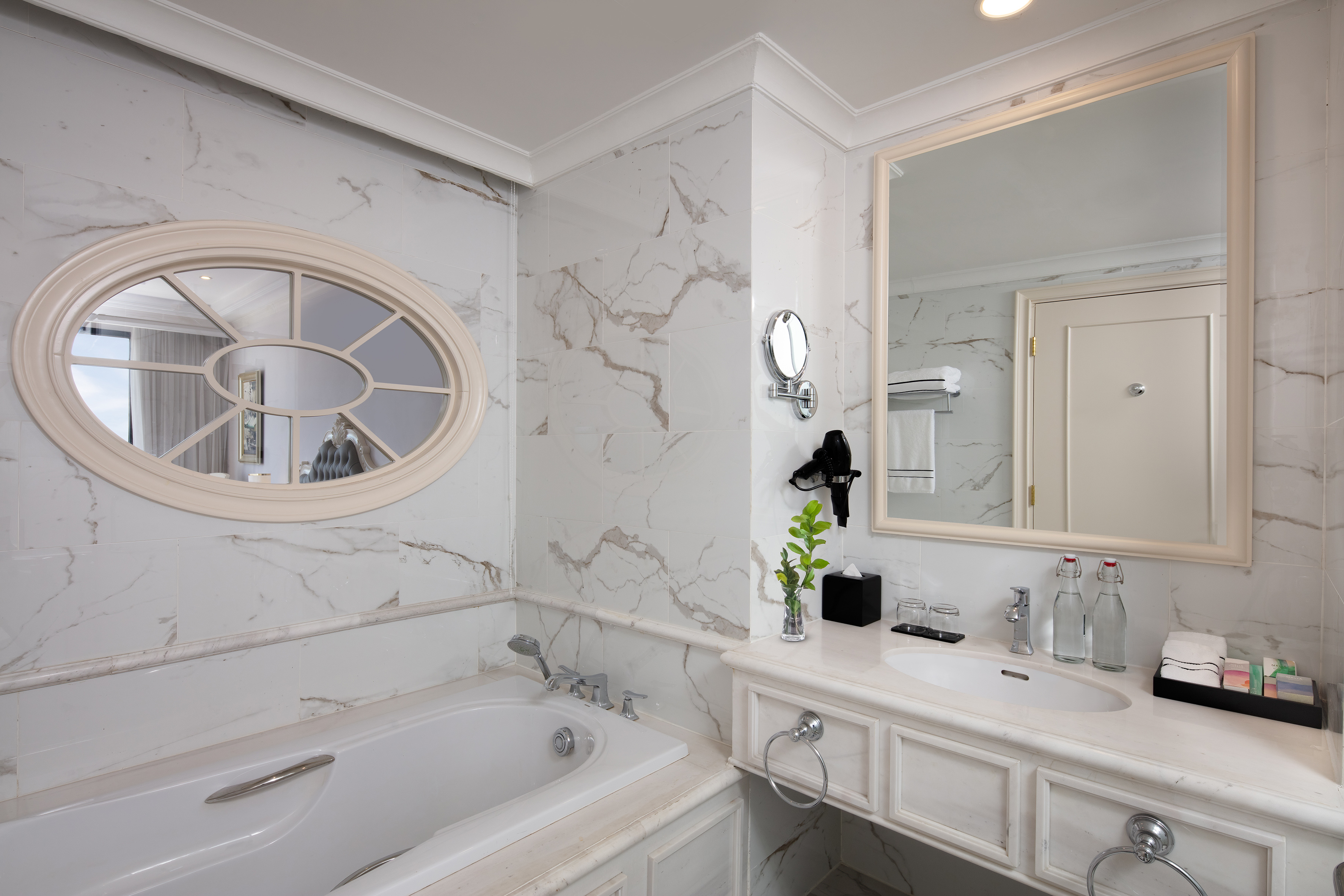 Elegant marble bathroom featuring a bathtub, oval mirror, and large vanity.