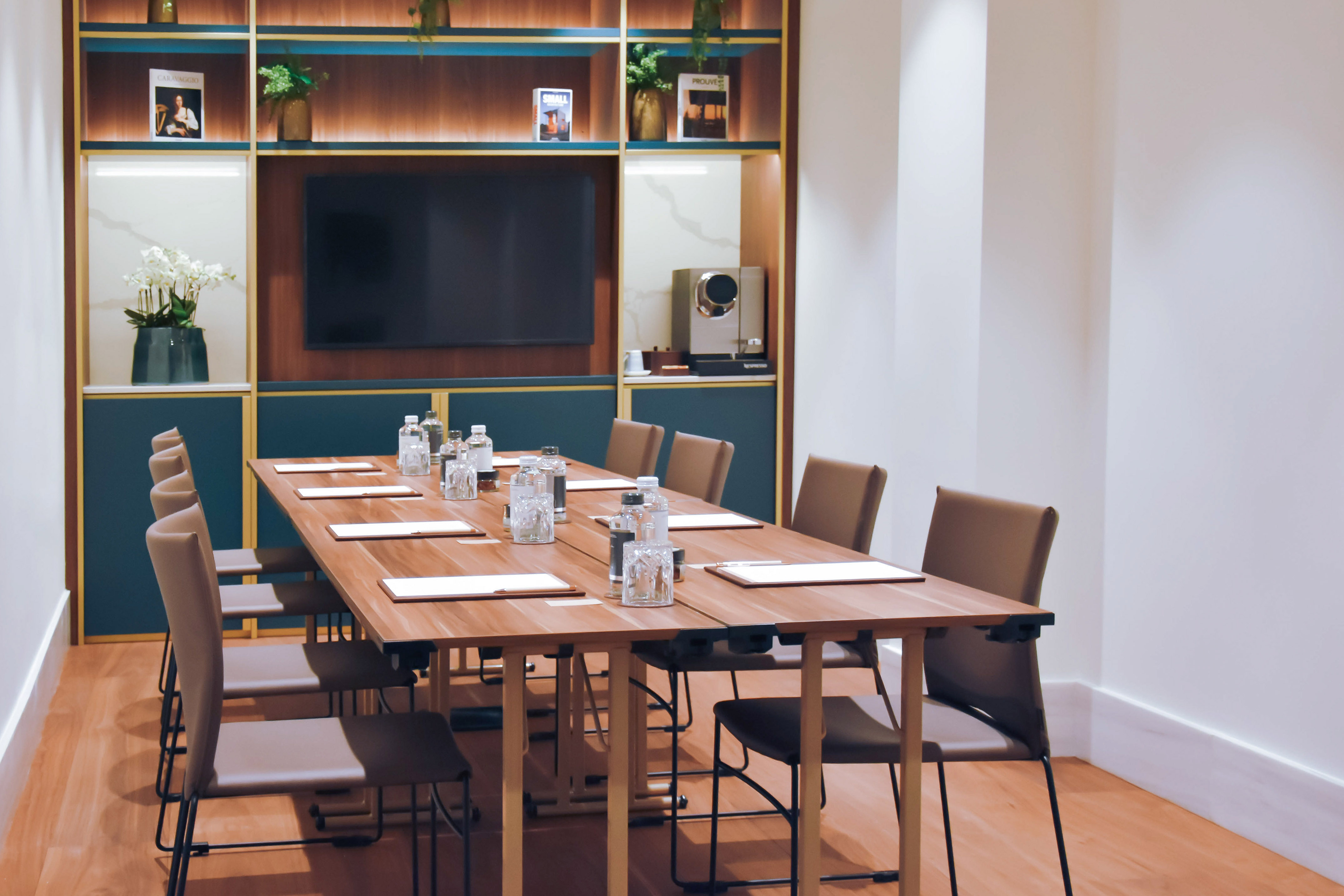 Modern conference room with wooden table, chairs, TV, and coffee station.