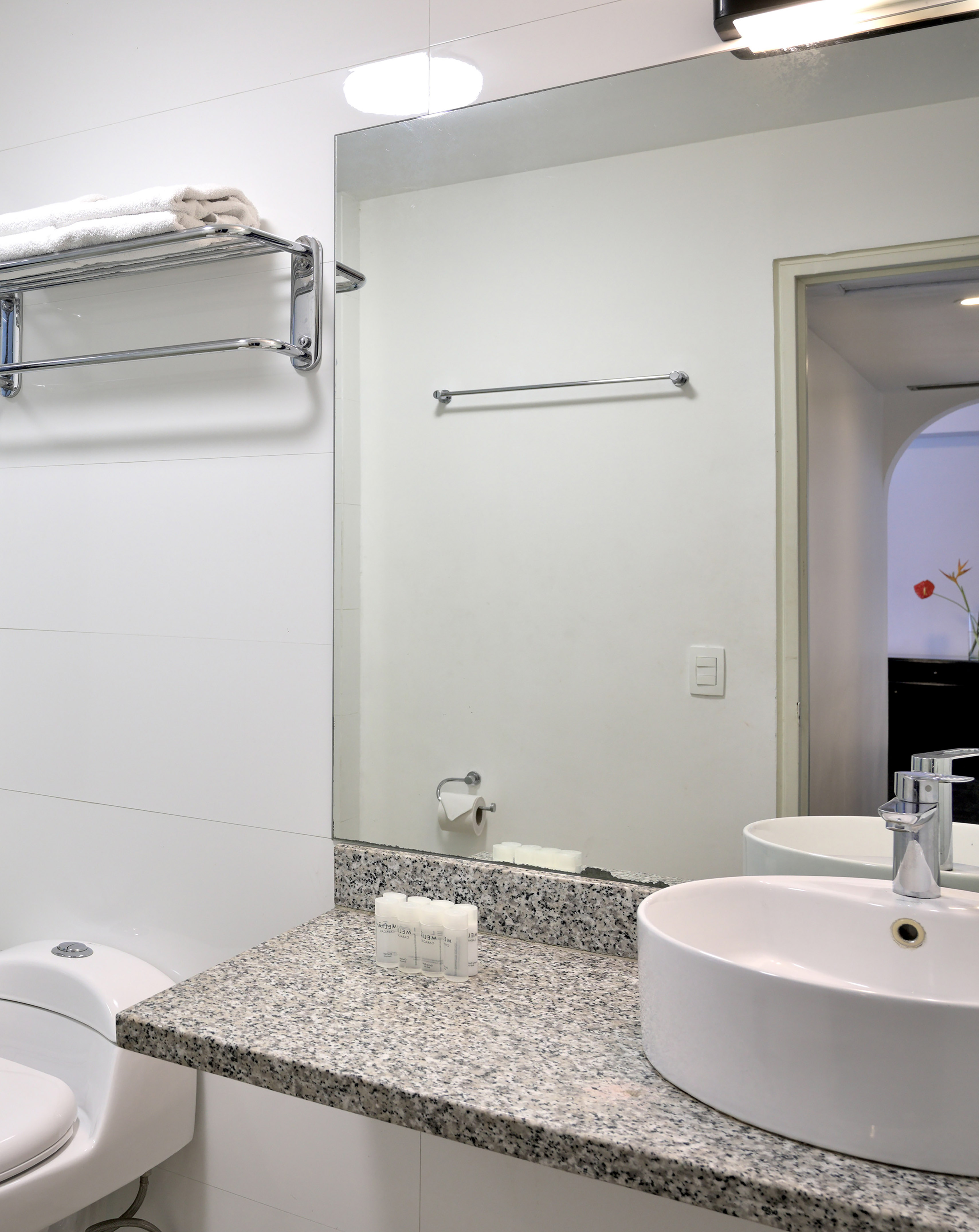 Bright hotel bathroom with vessel sink, granite counter, toilet, towels, toiletries.