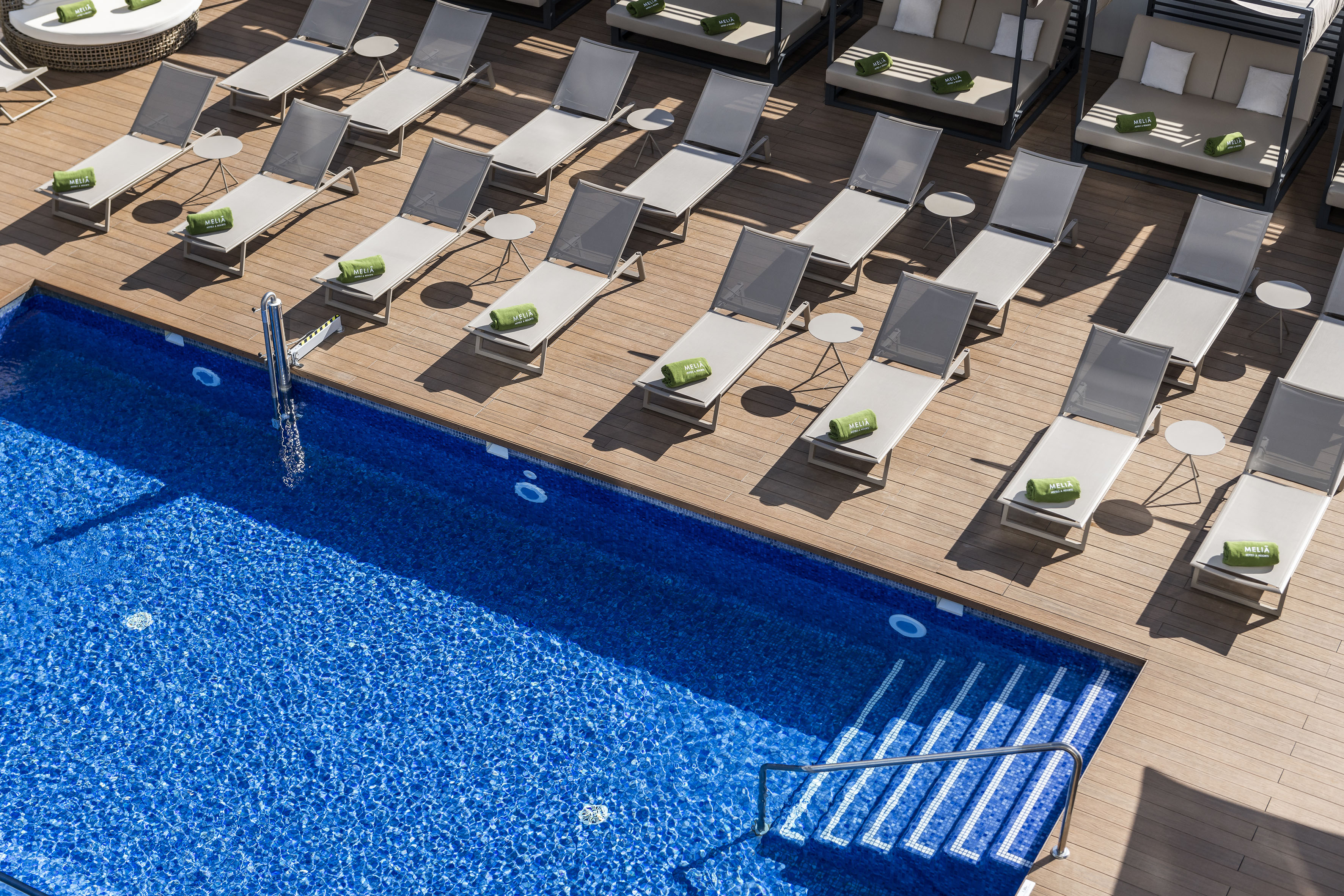Meliá hotel pool with wooden deck, sun loungers, and green towels.