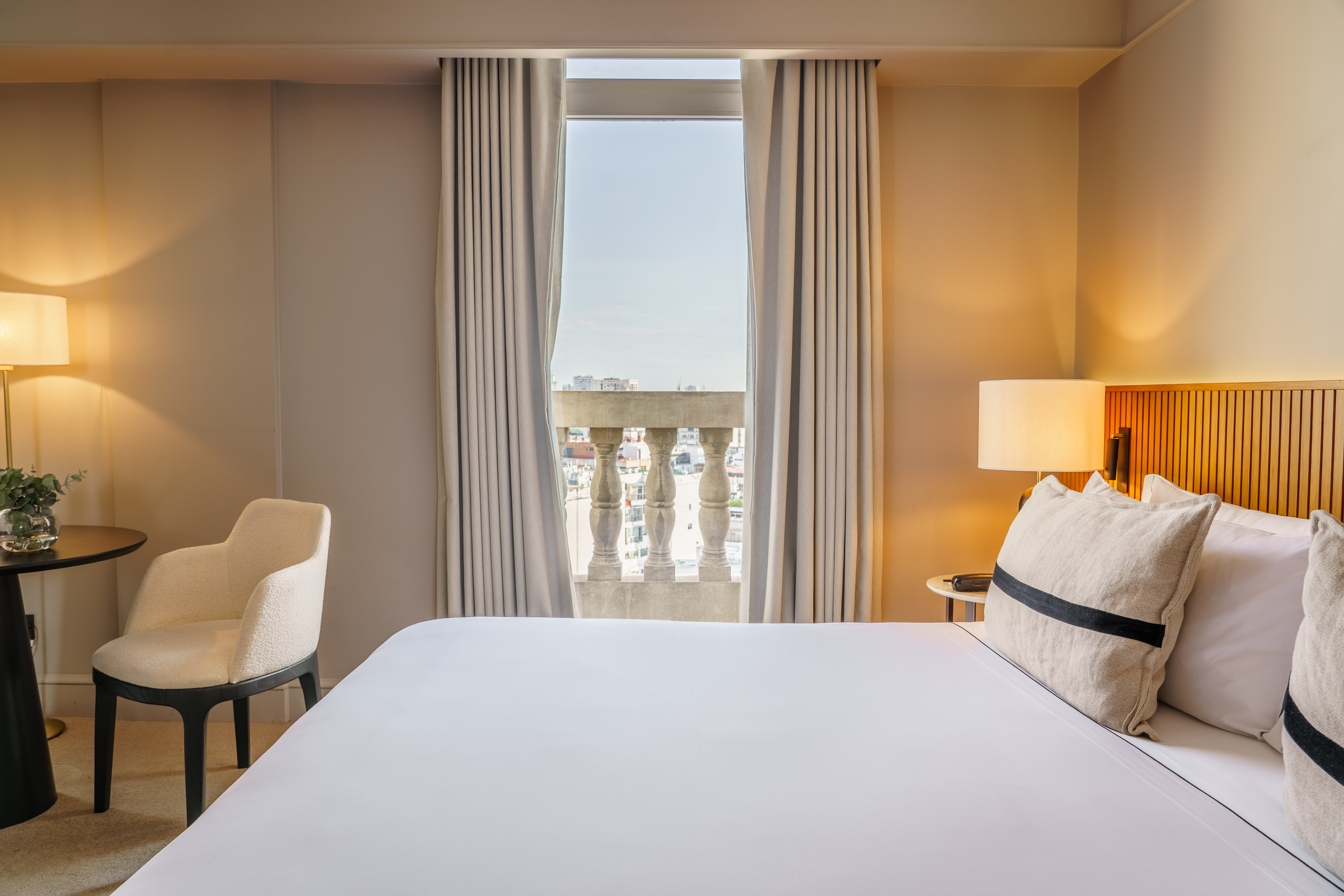 Modern hotel bedroom with balcony, city view, and warm lighting.