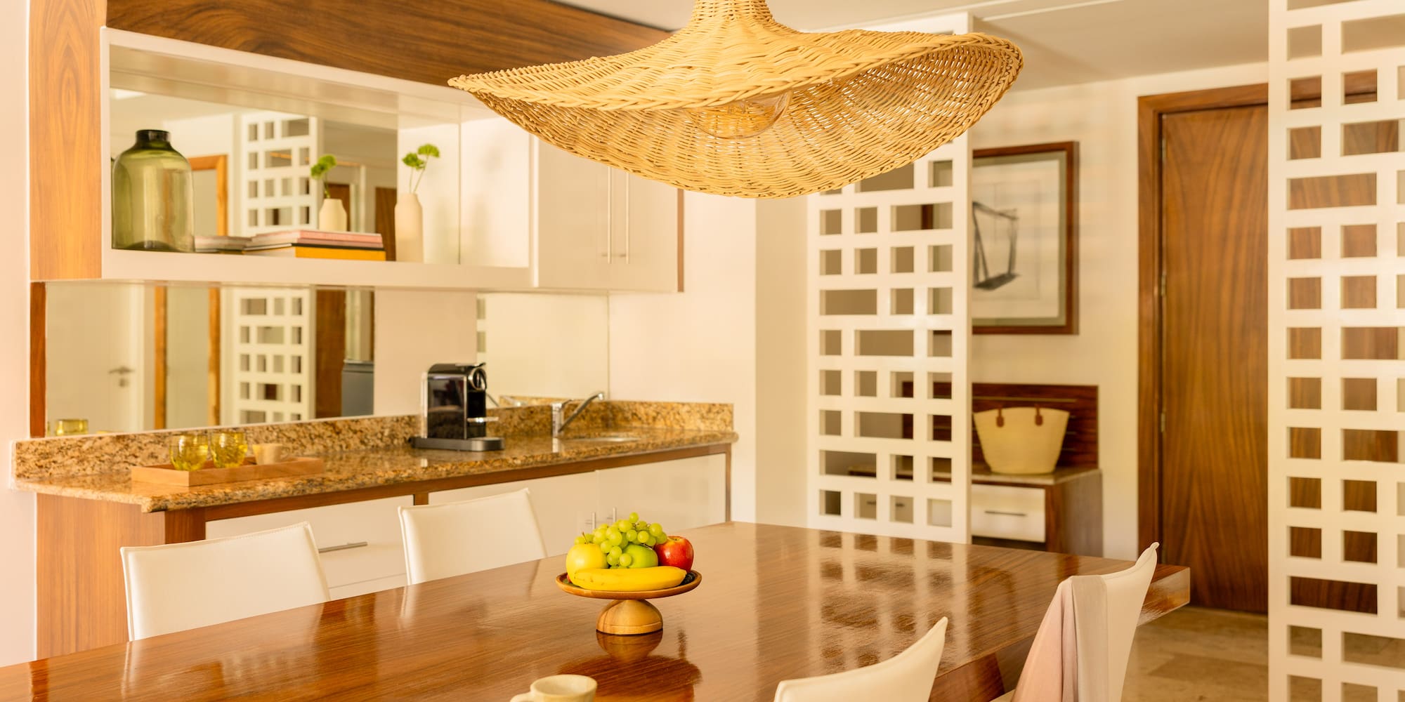 Dining room with modern wooden table, fruit bowl, and woven straw pendant light.