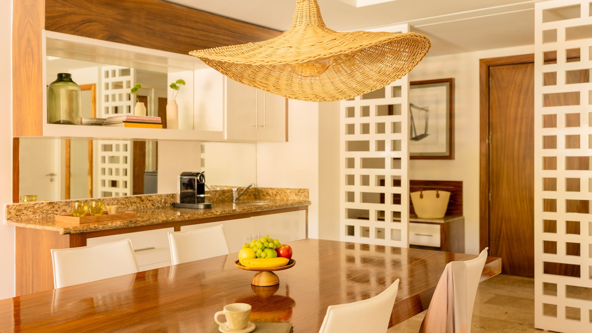 Dining room with modern wooden table, fruit bowl, and woven straw pendant light.