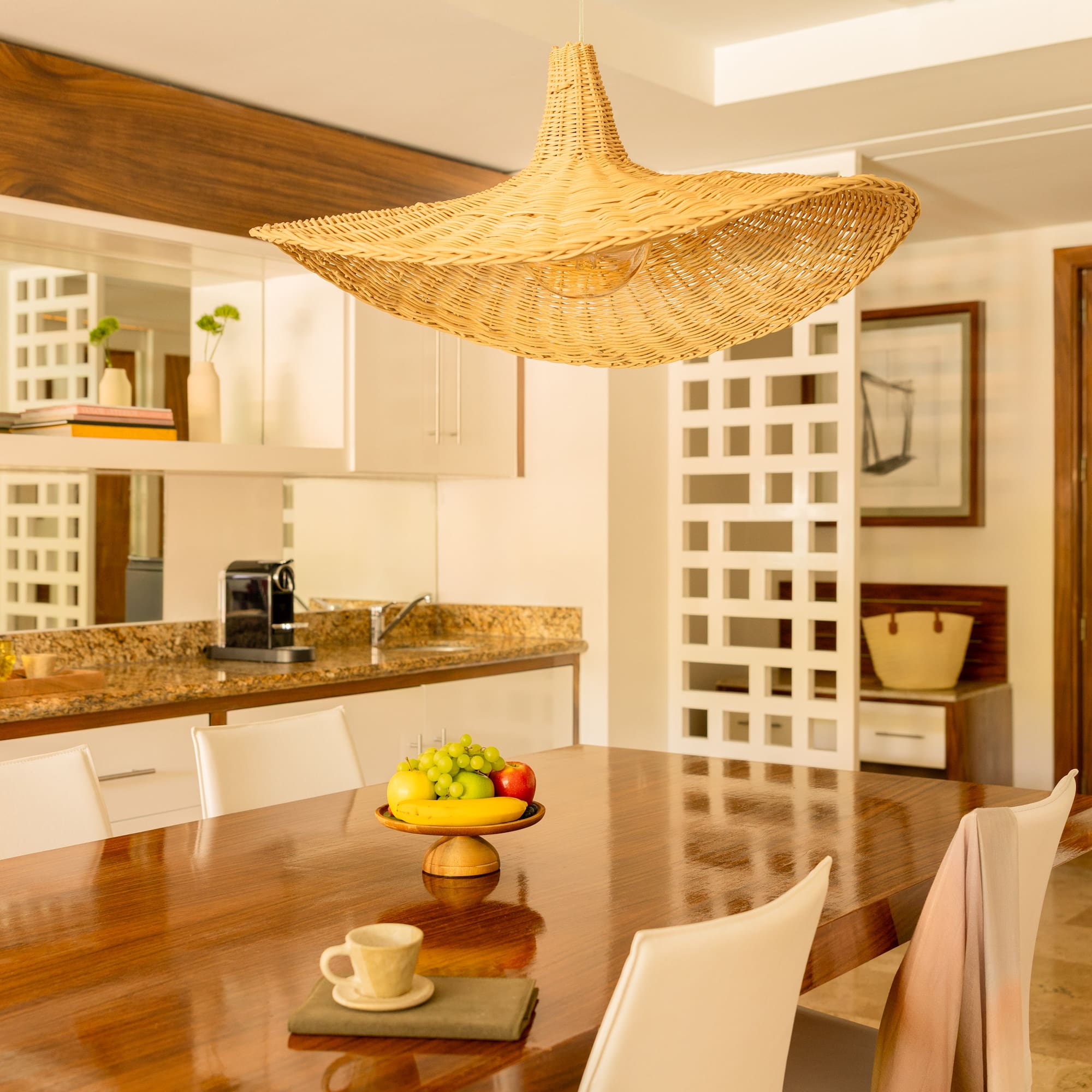 Dining room with modern wooden table, fruit bowl, and woven straw pendant light.