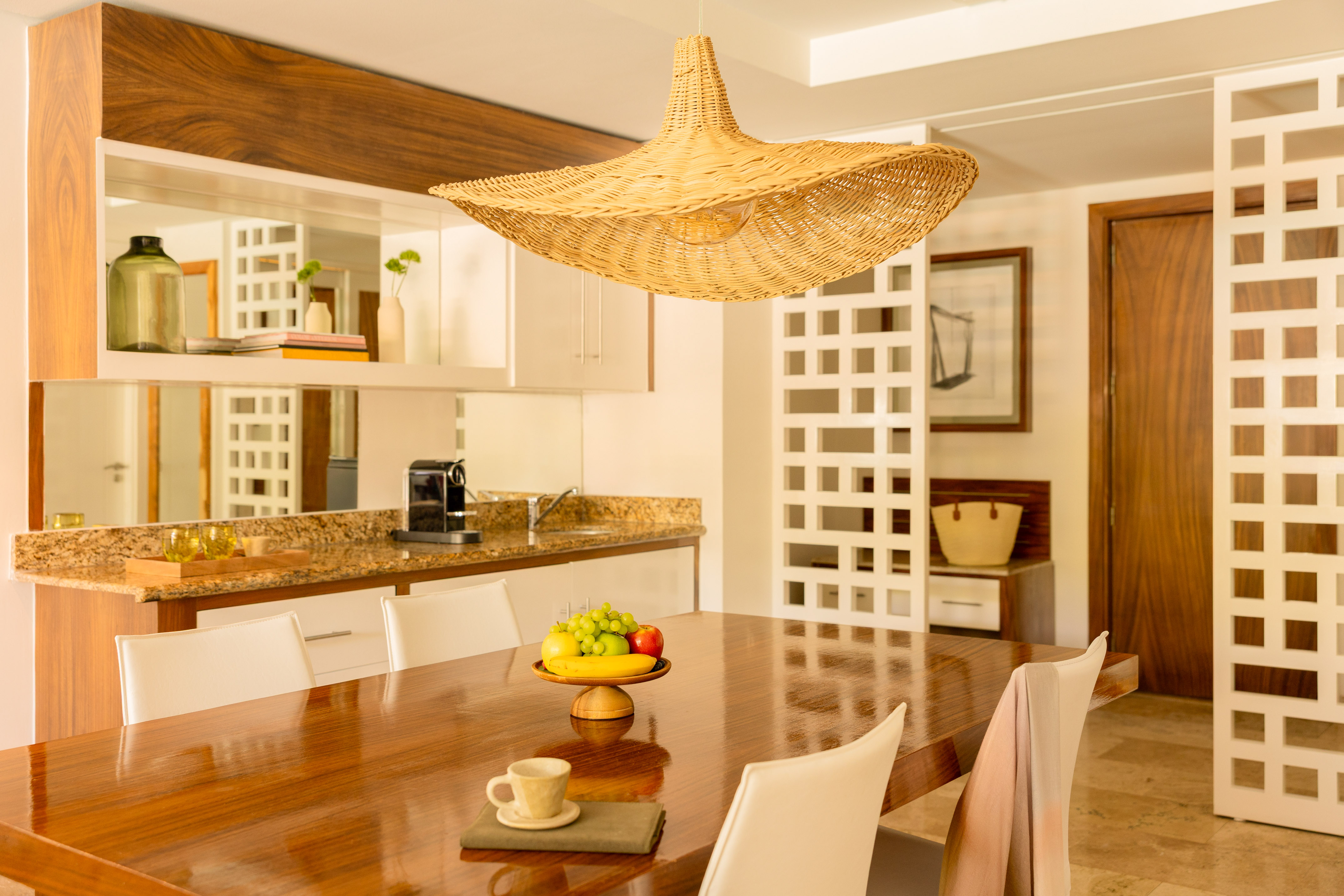 Dining room with modern wooden table, fruit bowl, and woven straw pendant light.