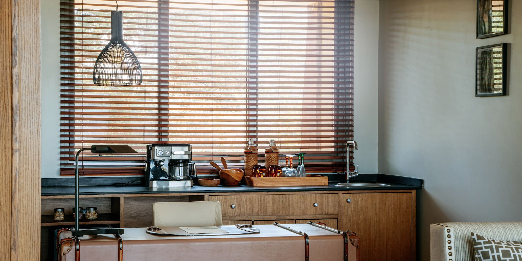 Modern home office with wet bar, coffee machine, leather desk, and wood blinds.