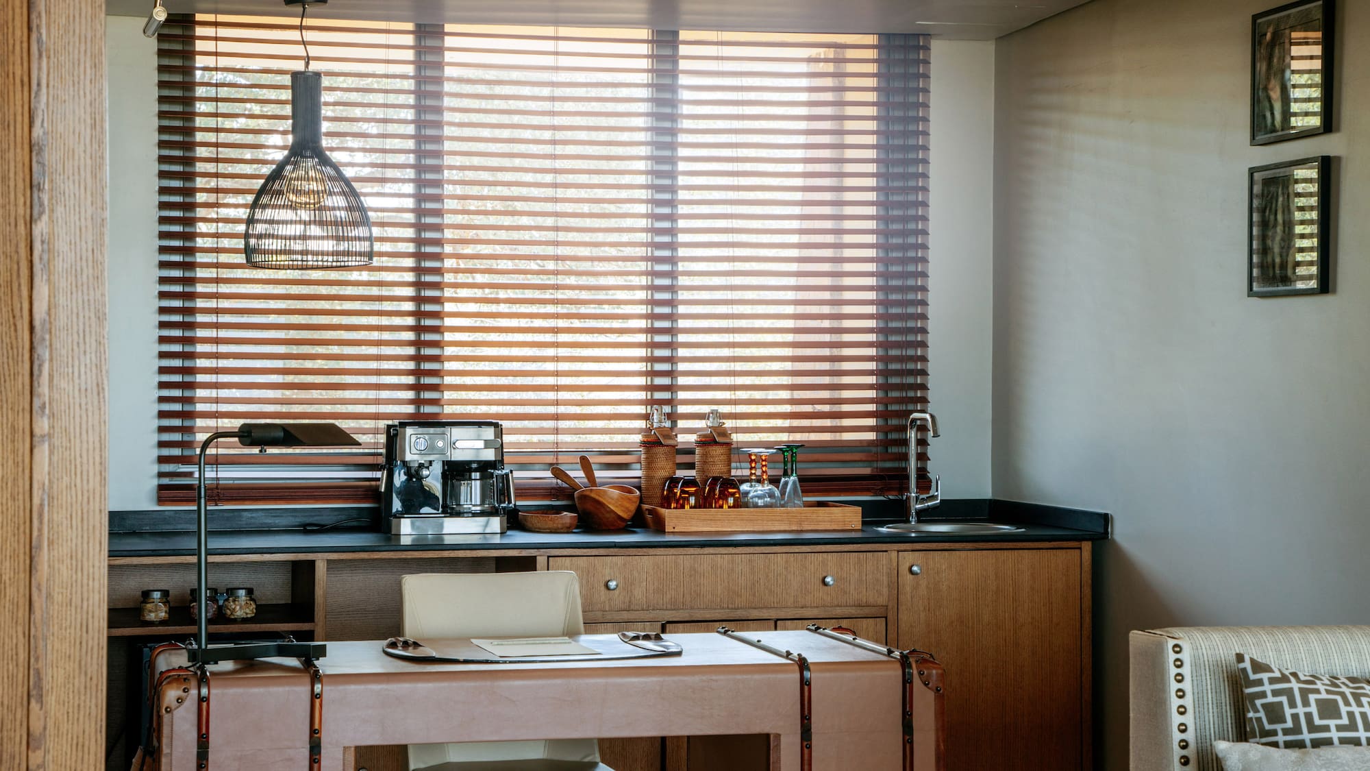 Modern home office with wet bar, coffee machine, leather desk, and wood blinds.