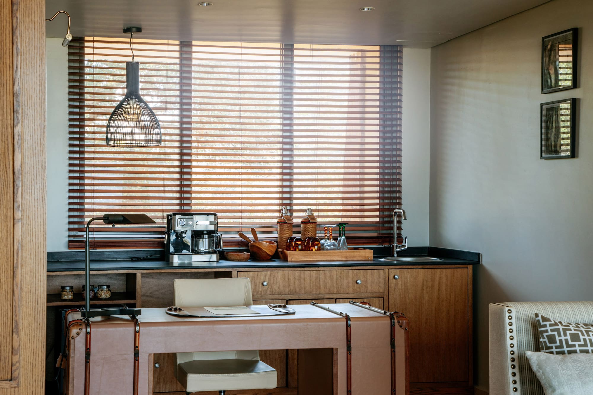 Modern home office with wet bar, coffee machine, leather desk, and wood blinds.