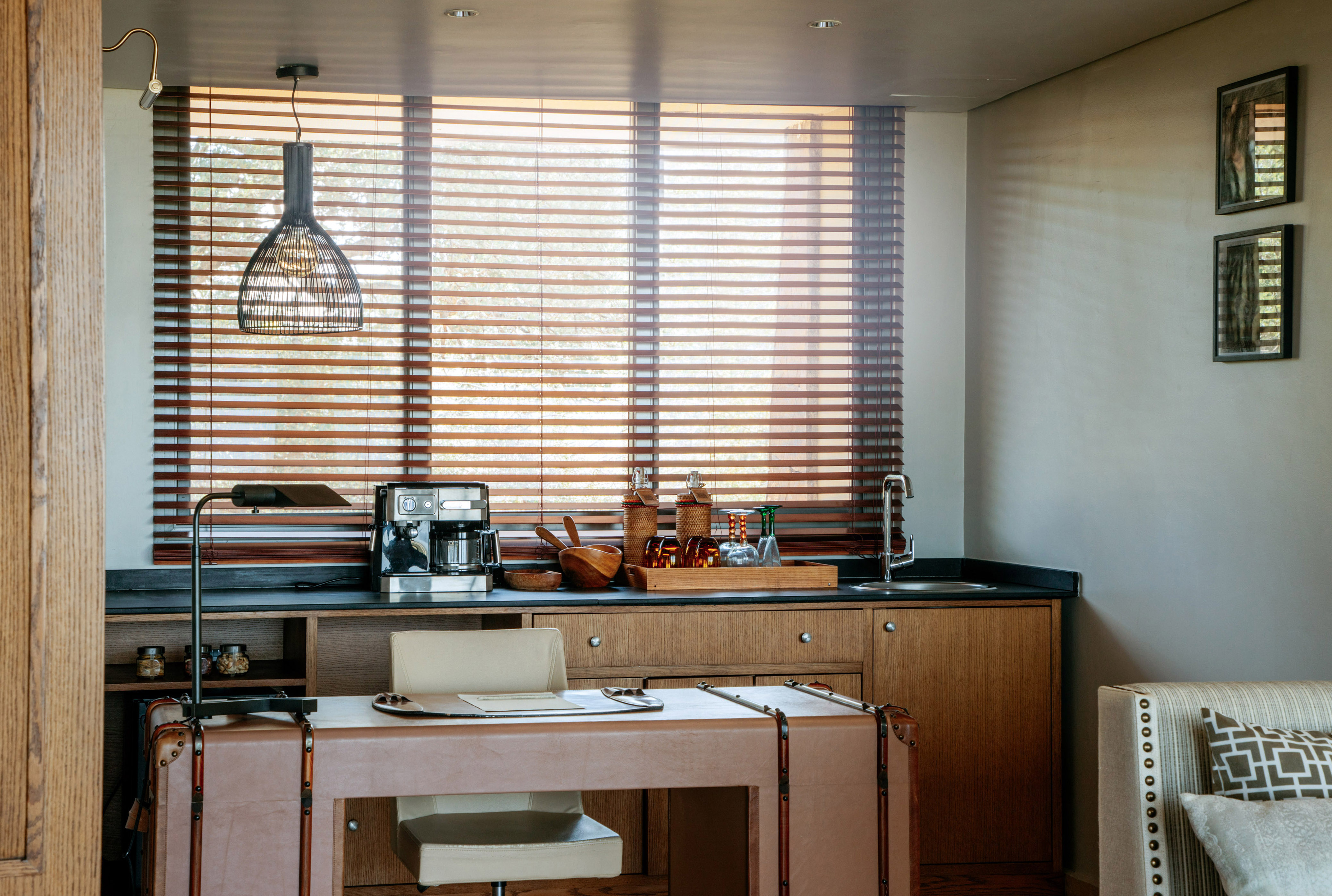 Modern home office with wet bar, coffee machine, leather desk, and wood blinds.