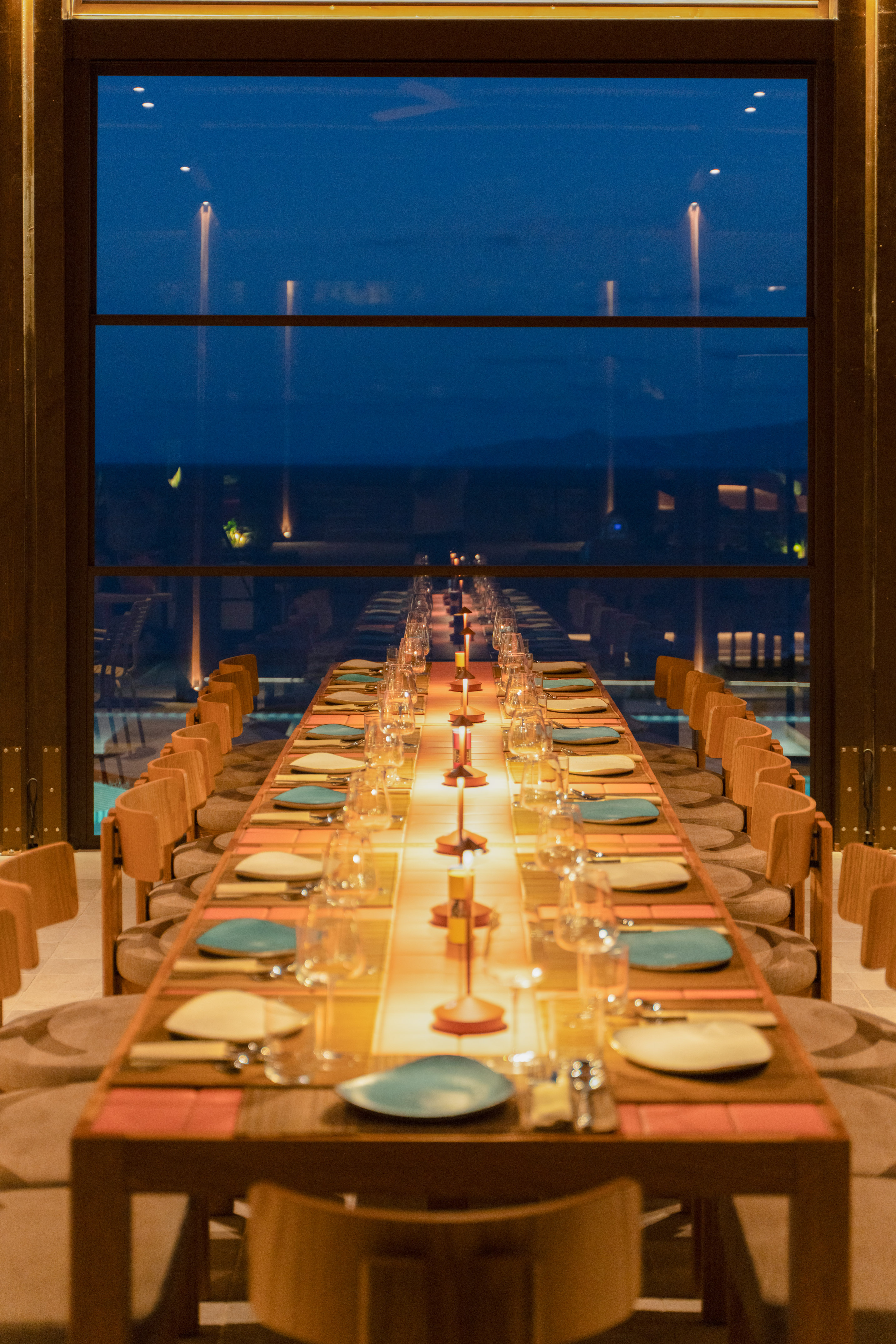 Elegant long dining table set with warm lighting against a dark night window.