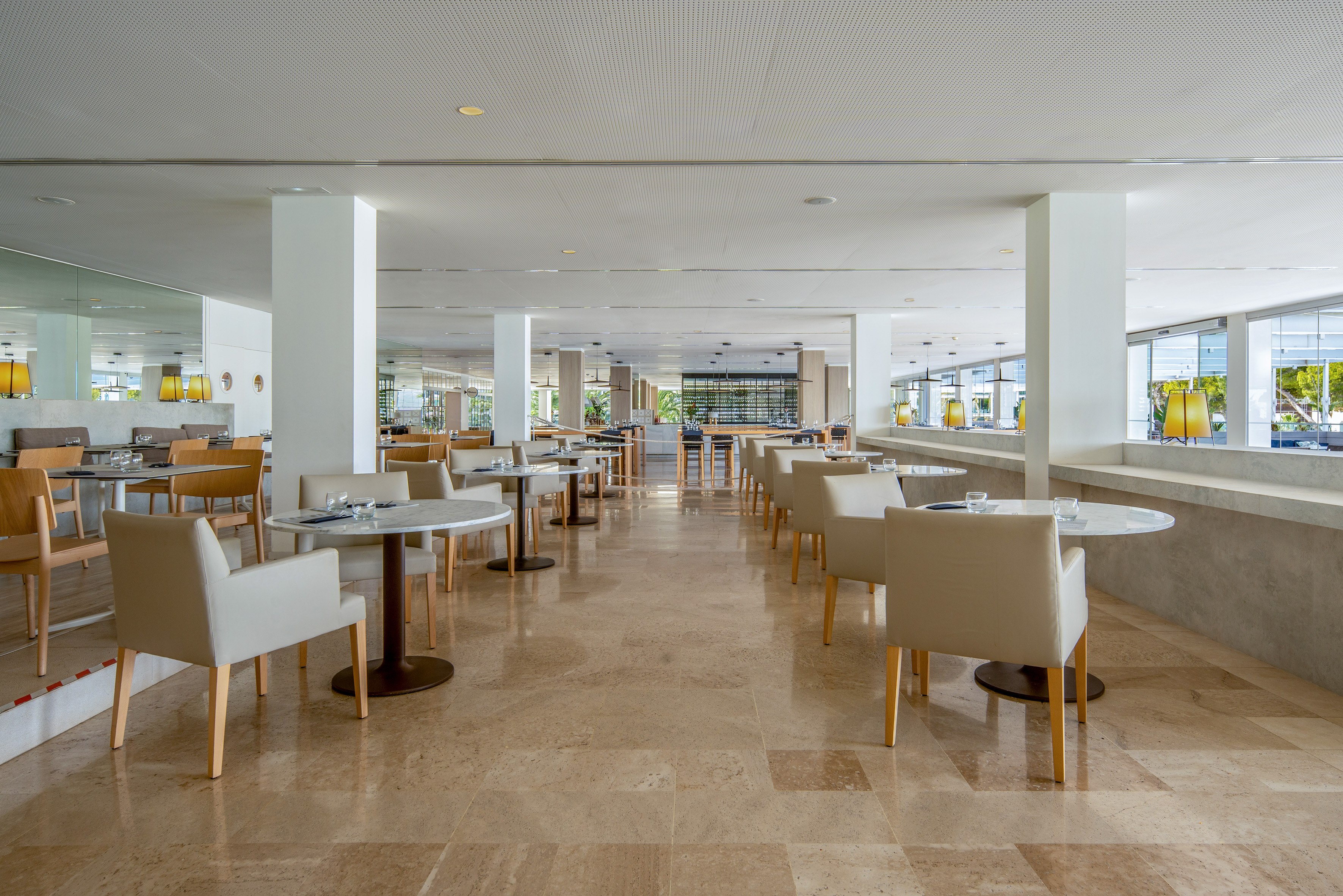 Bright, modern hotel restaurant interior with tables, chairs, and marble flooring.