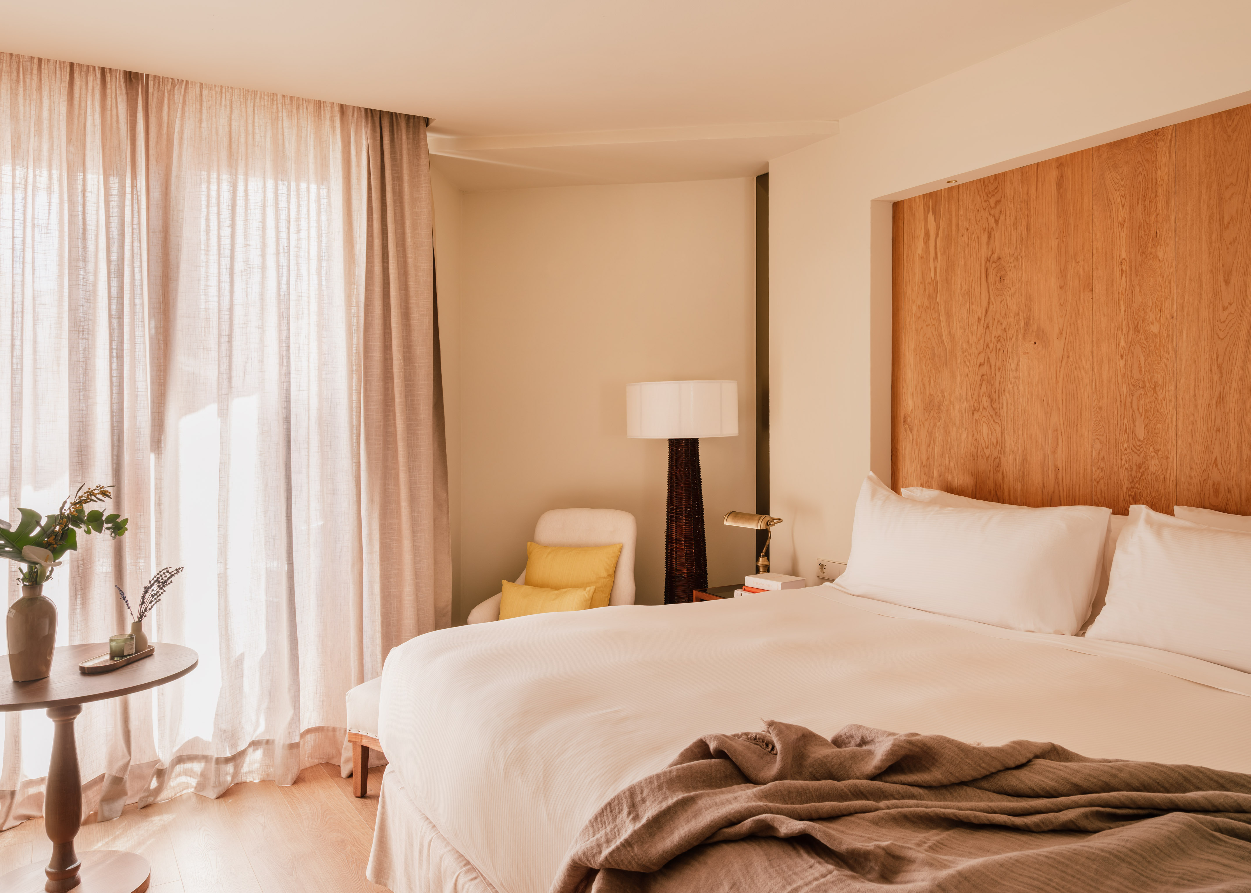 Bright bedroom with bed, wooden headboard, sheer curtains, and natural light.