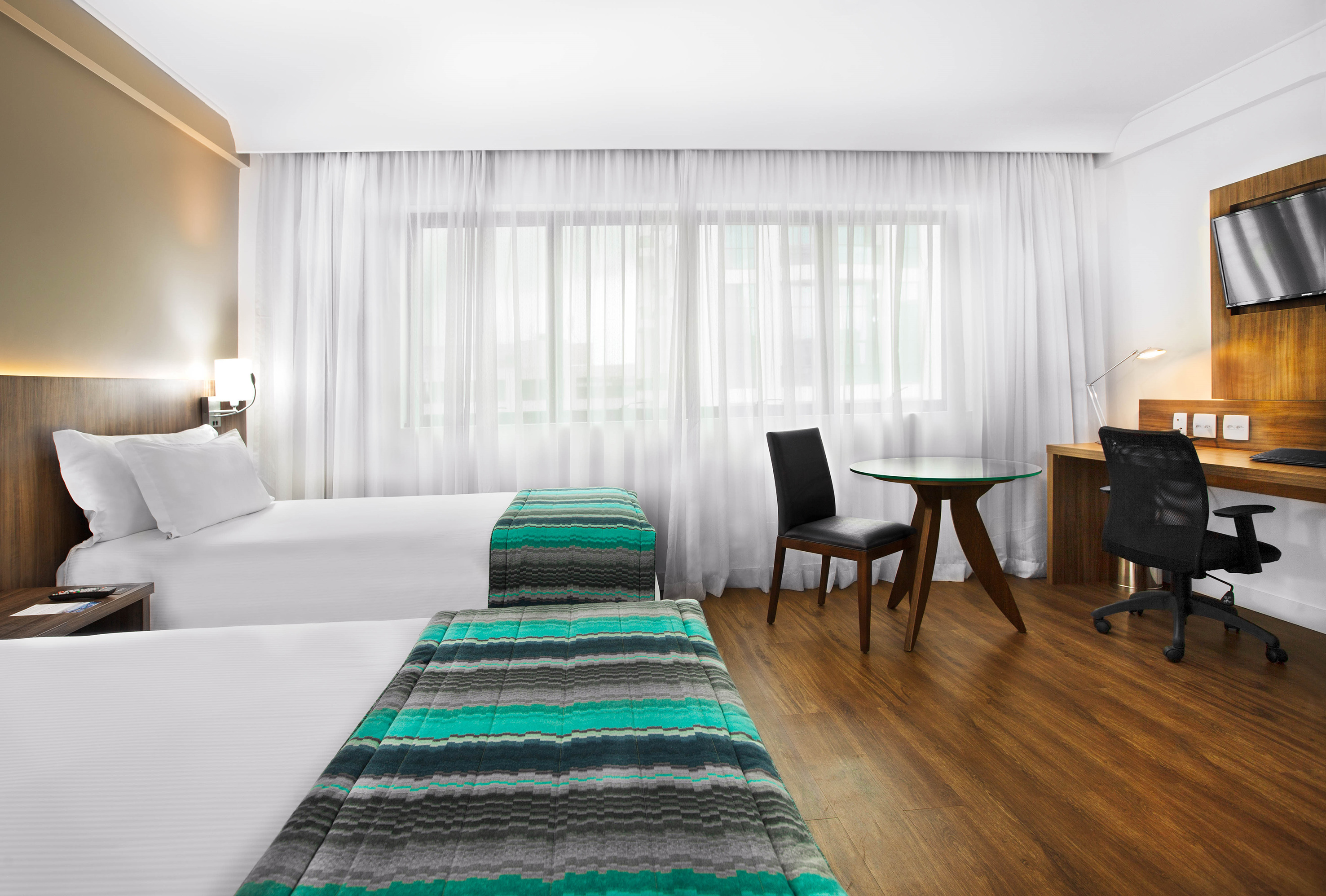 Contemporary hotel twin room with two beds, work desk, and large window.