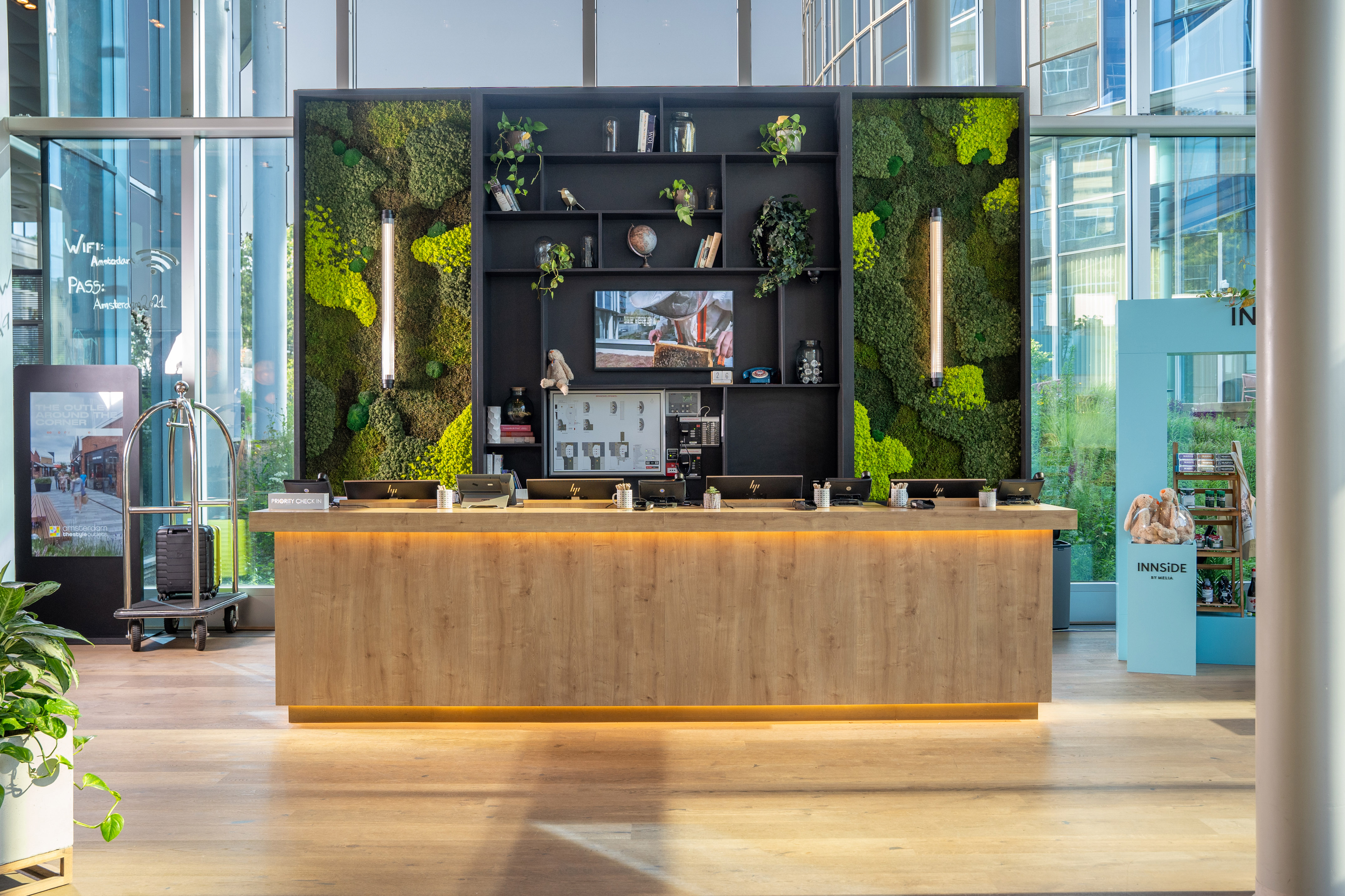 Innside hotel reception with wooden desk, green moss wall, and modern design.