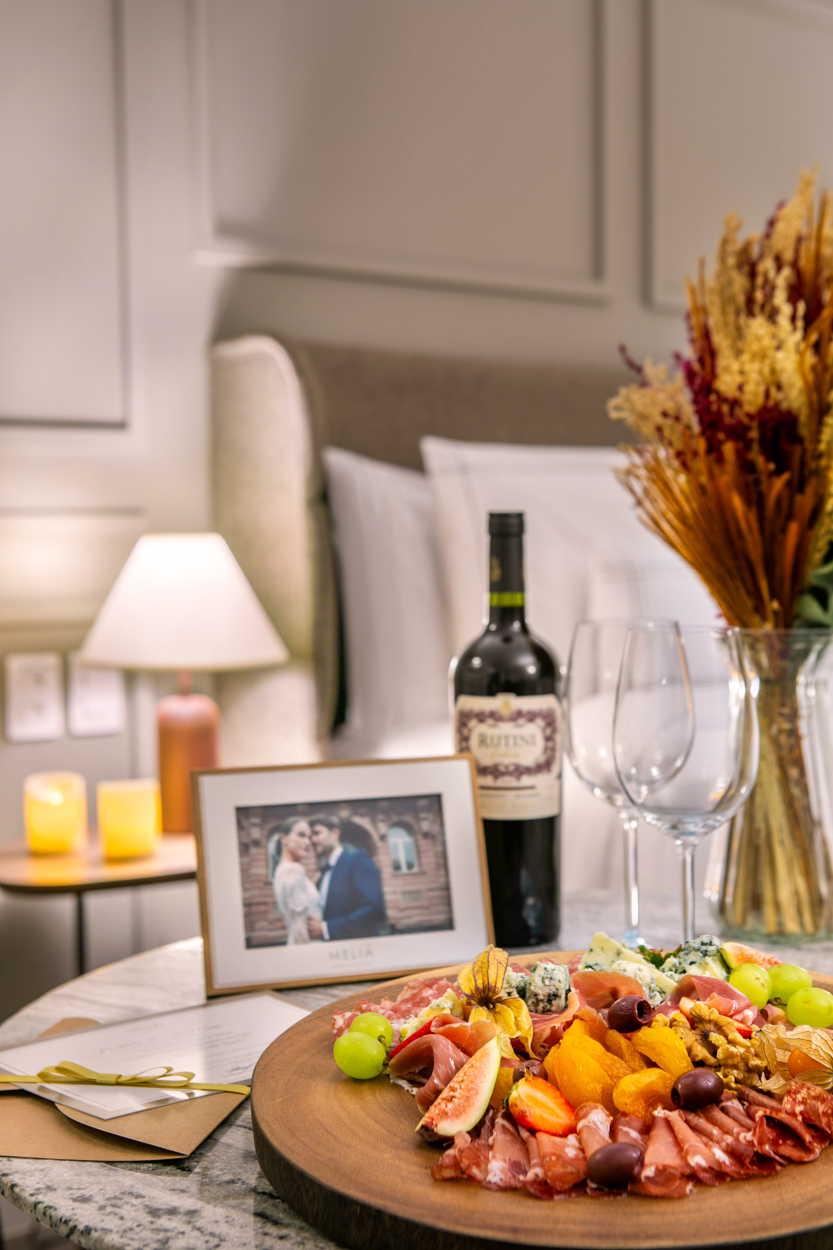 Romantic charcuterie board with wine, cheeses, cured meats, and fruits in a hotel room.