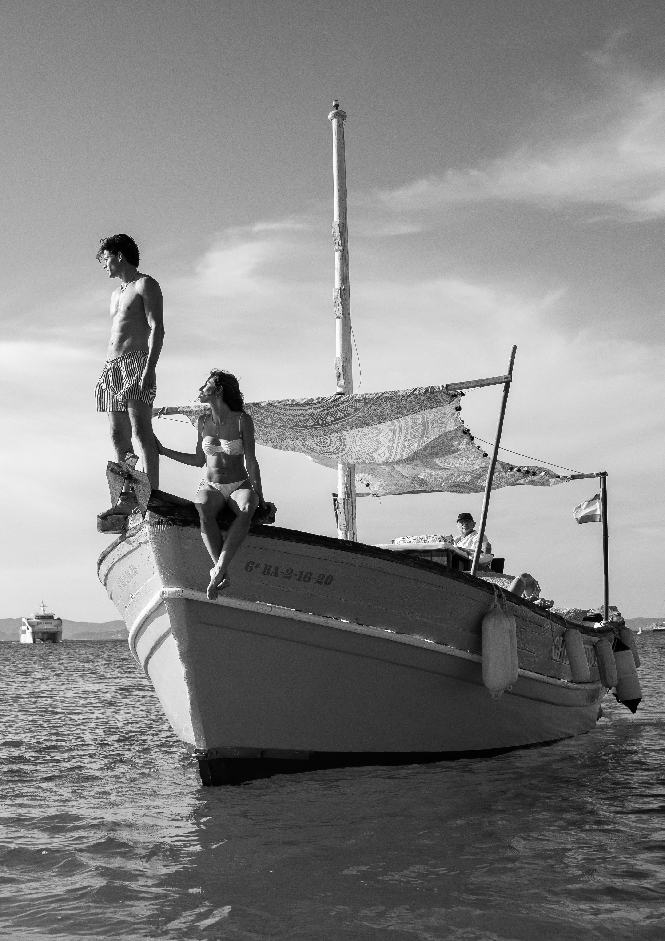 B&W; man standing, woman sitting on boat bow, ocean. Summer vacation.