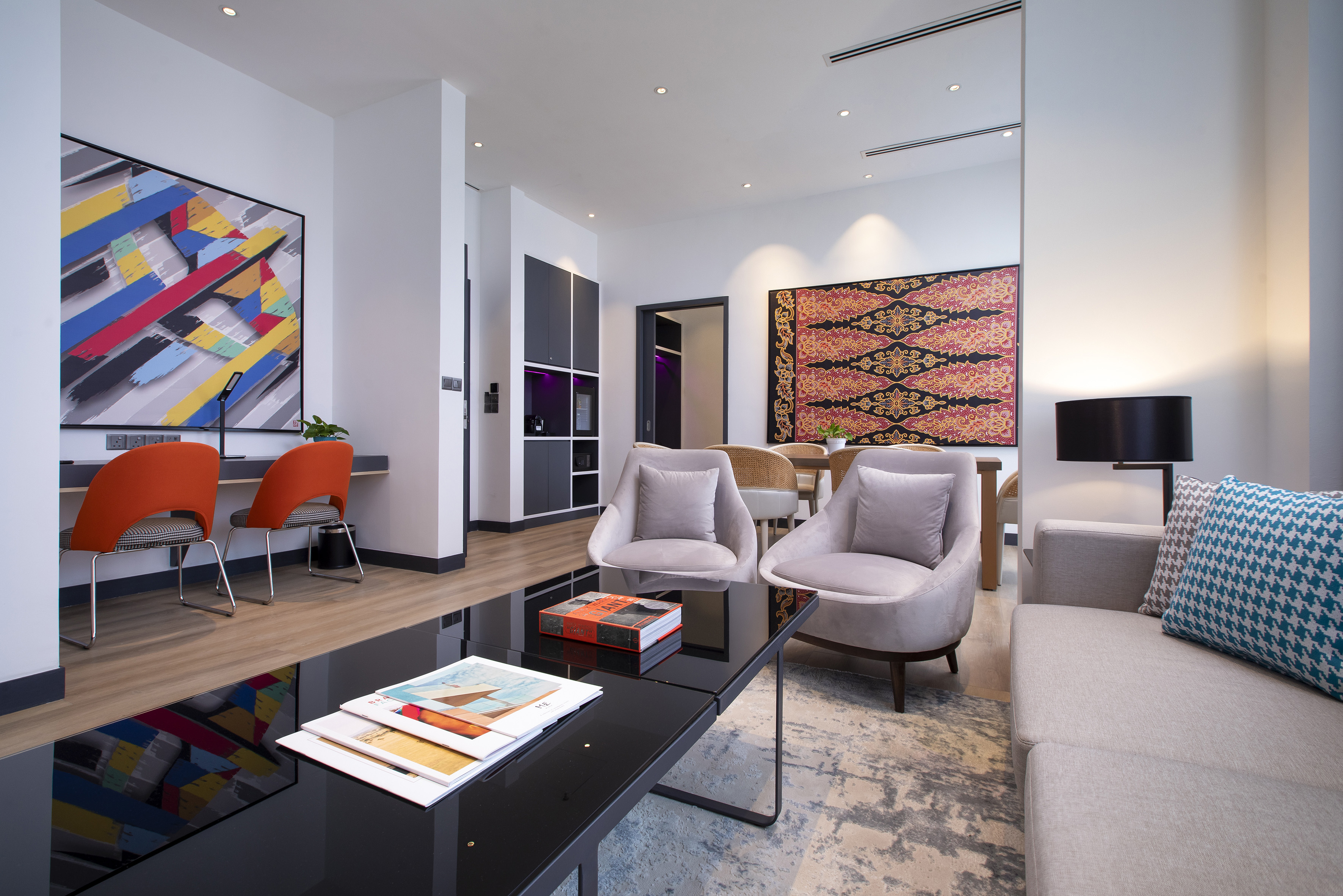 Modern living room with abstract art, orange chairs, sofa, and dining space.