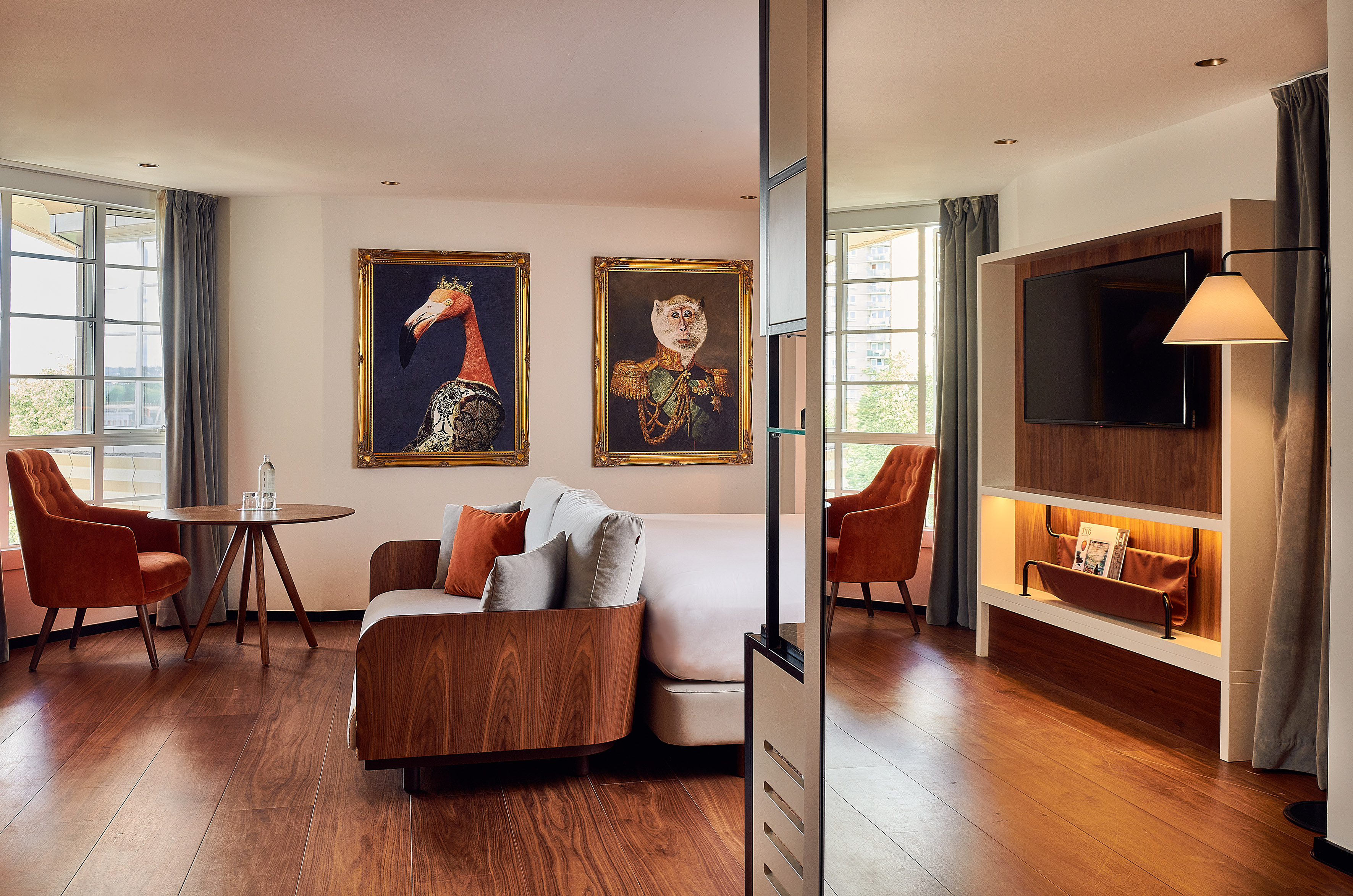 Modern hotel room with bed, sofa, hardwood floor, TV, and quirky animal art.